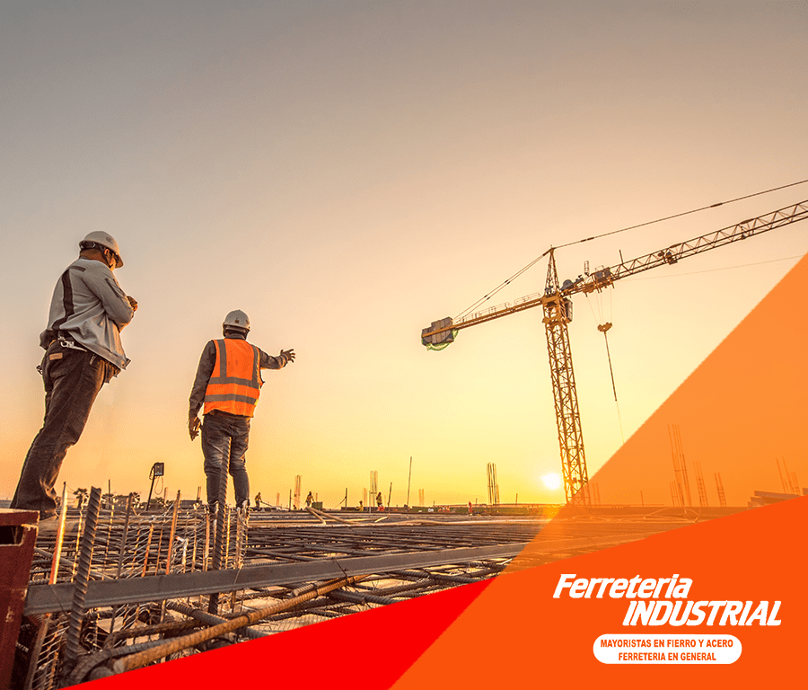 Obreros de la construcción en la obra con una grúa al atardecer. Chaleco naranja, casco y hormigón.