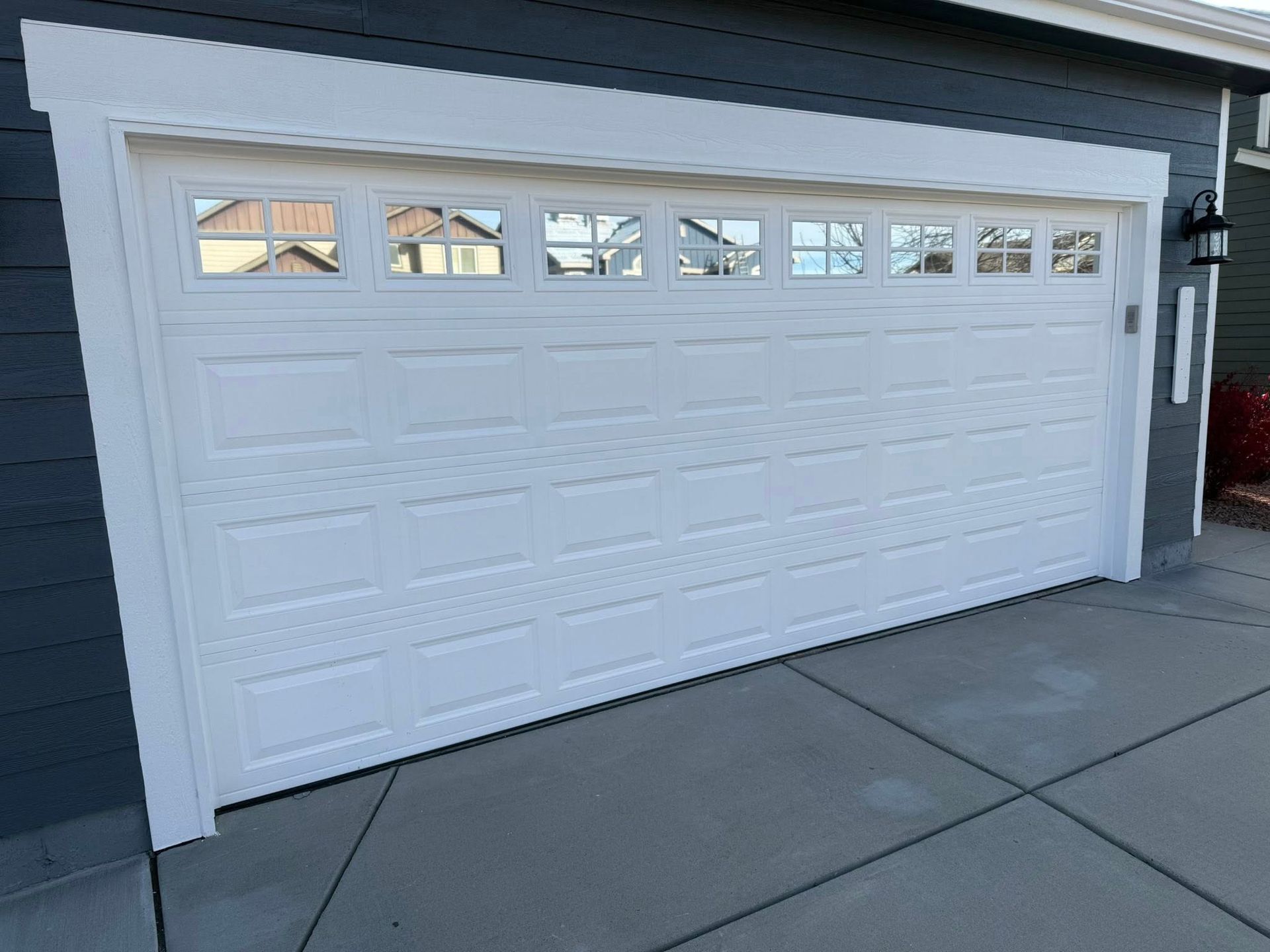A white garage door with rectangular window panels set in a dark gray house exterior.