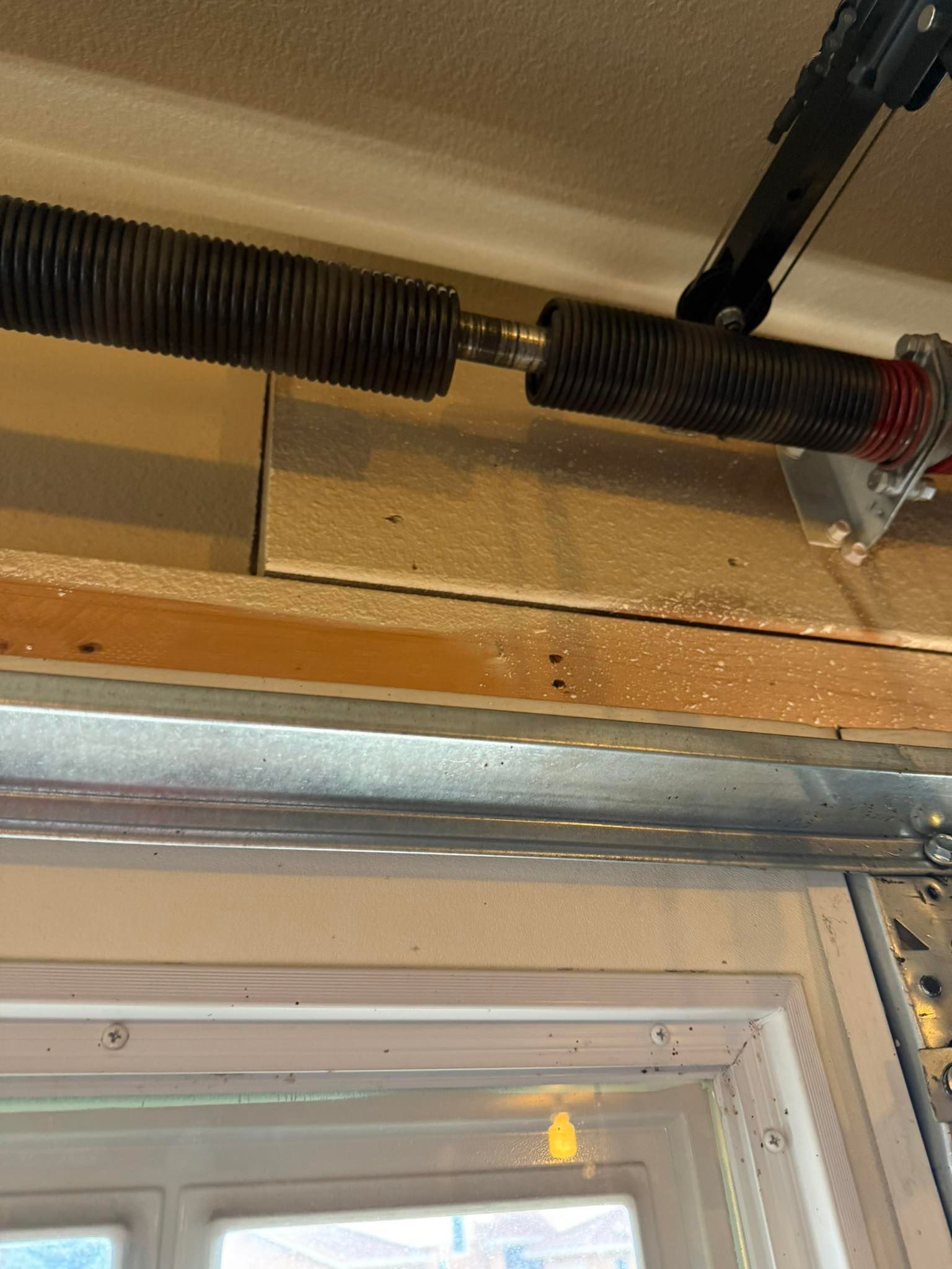 A broken, separated torsion spring mounted above a residential garage door frame.