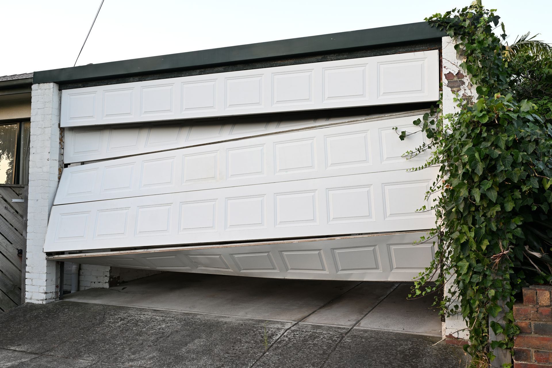 A white sectional garage door is broken and hanging at an angle while partially open.