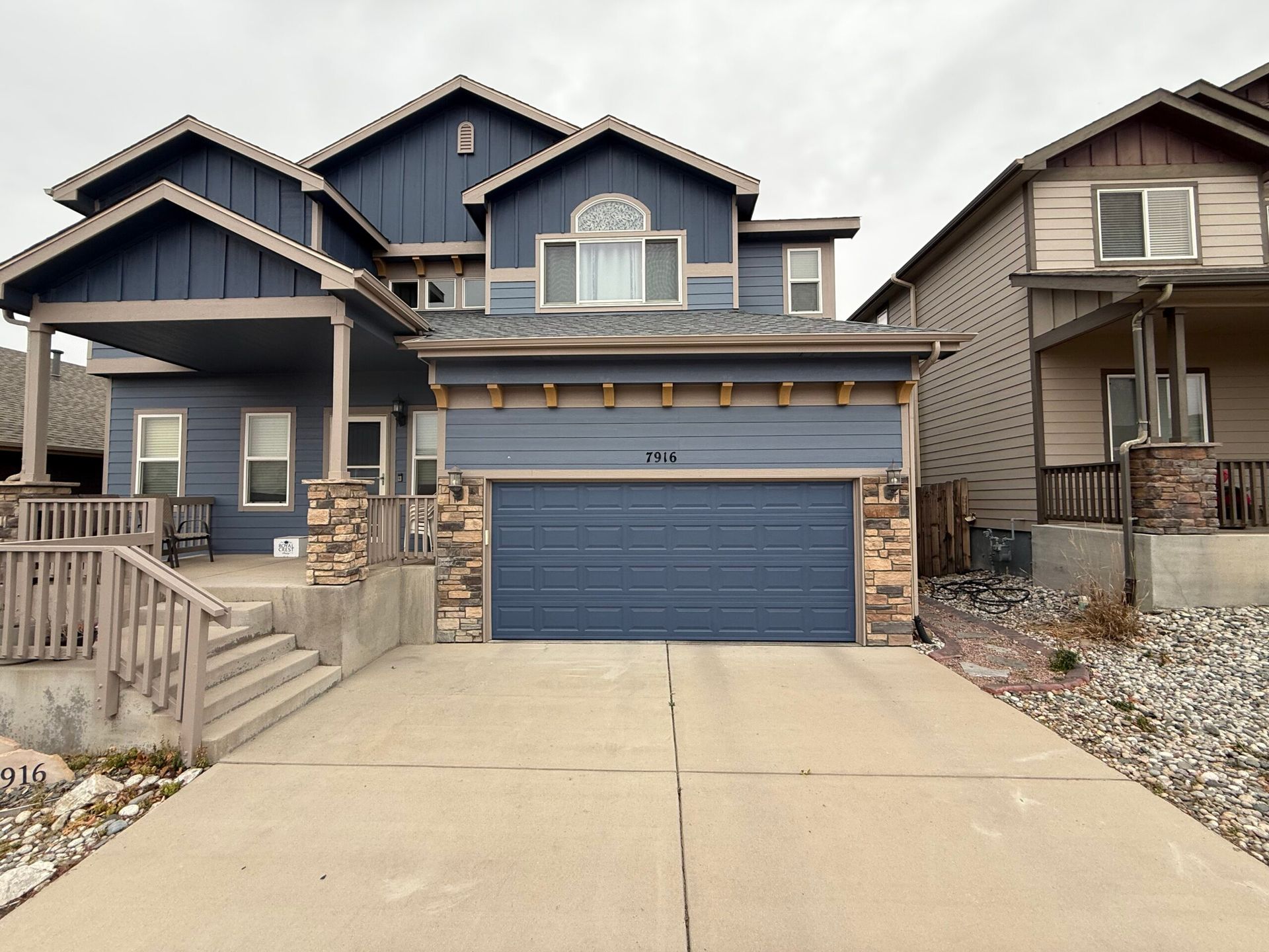 A two-story blue house with a stone-accented front porch, a wide garage door, and a concrete driveway.