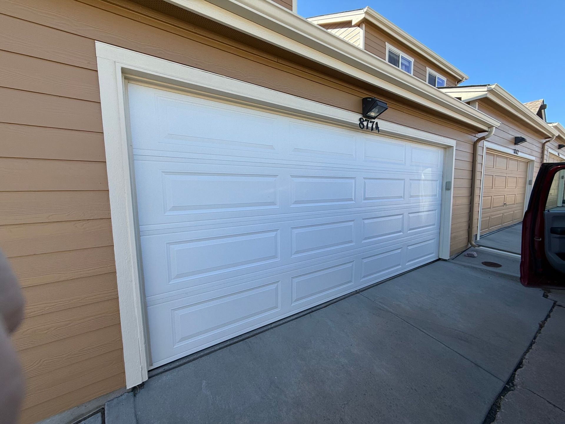 A white garage door on a tan house with a concrete driveway on a sunny day.