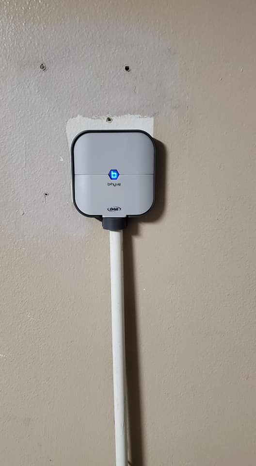 A small device is attached to a white pipe on a wall.