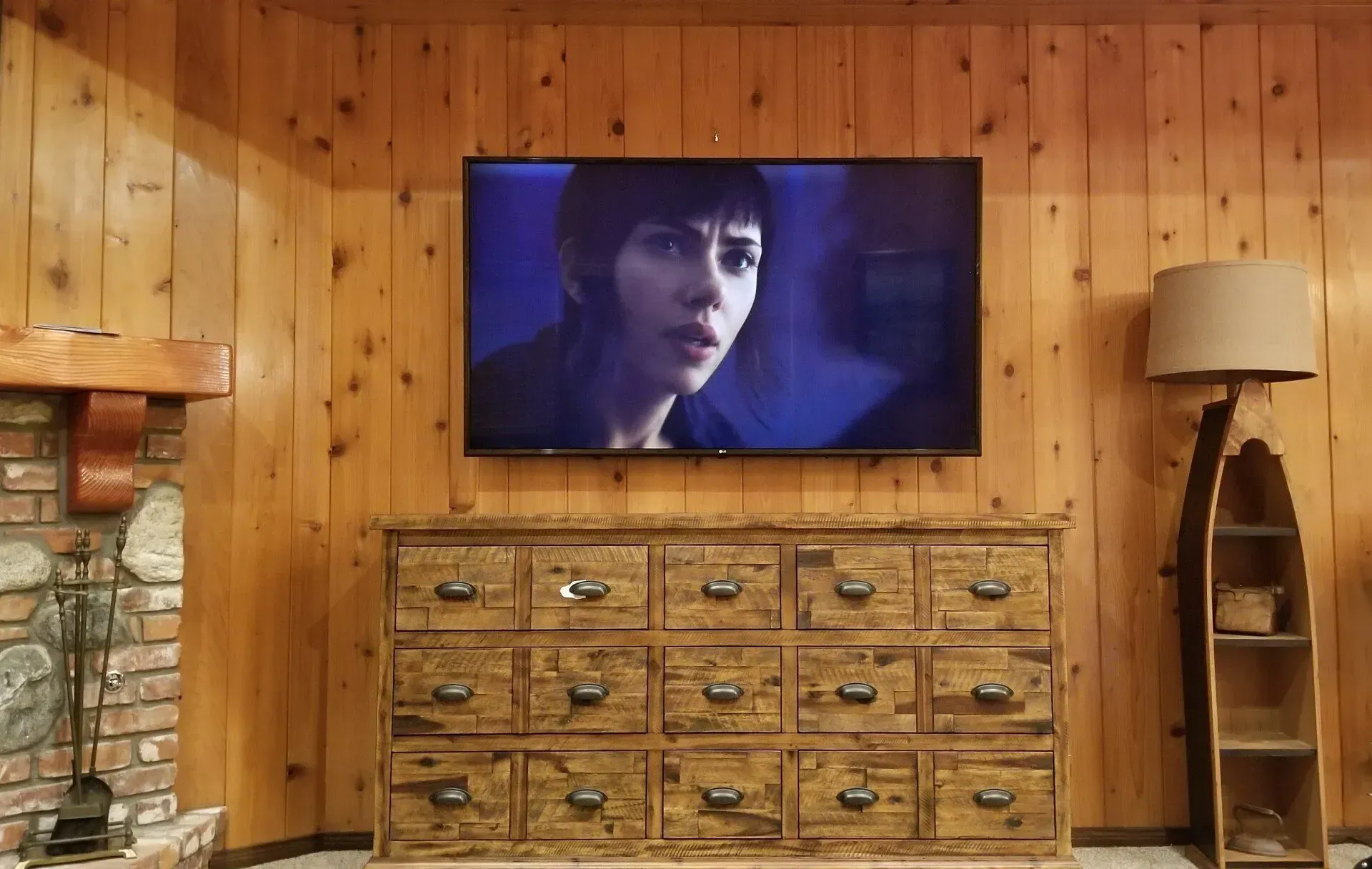 A flat screen tv is hanging on a wooden wall above a wooden dresser.