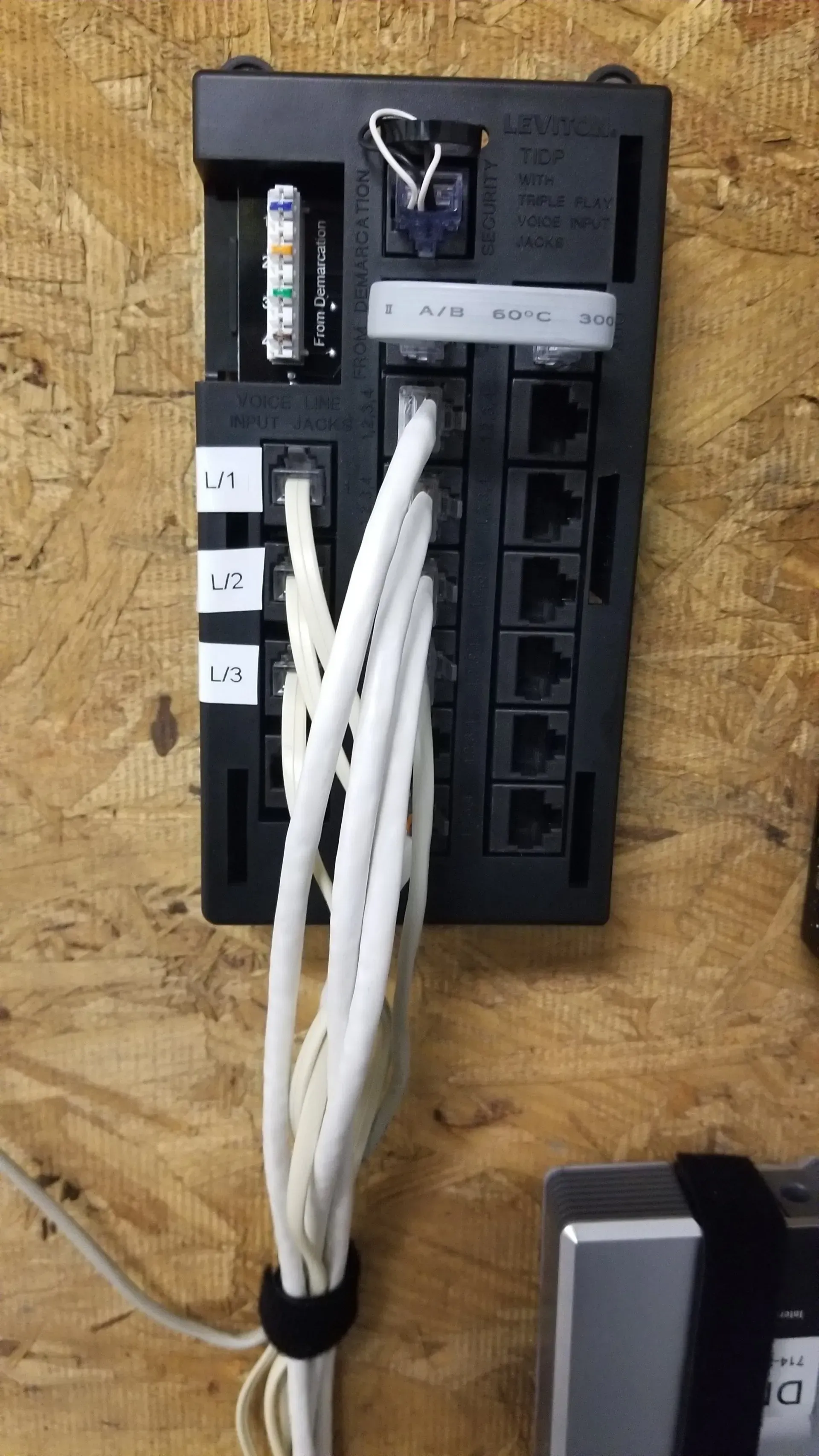 A bunch of wires are connected to a black box on a wooden wall.