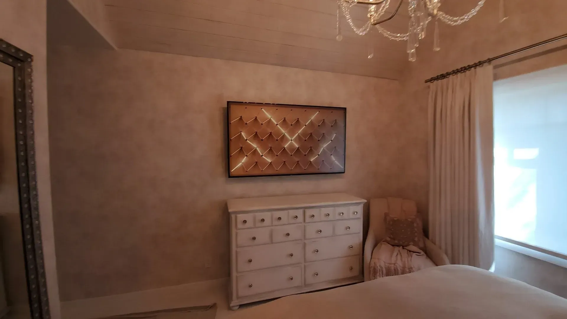 A bedroom with a bed , dresser , mirror and chandelier.