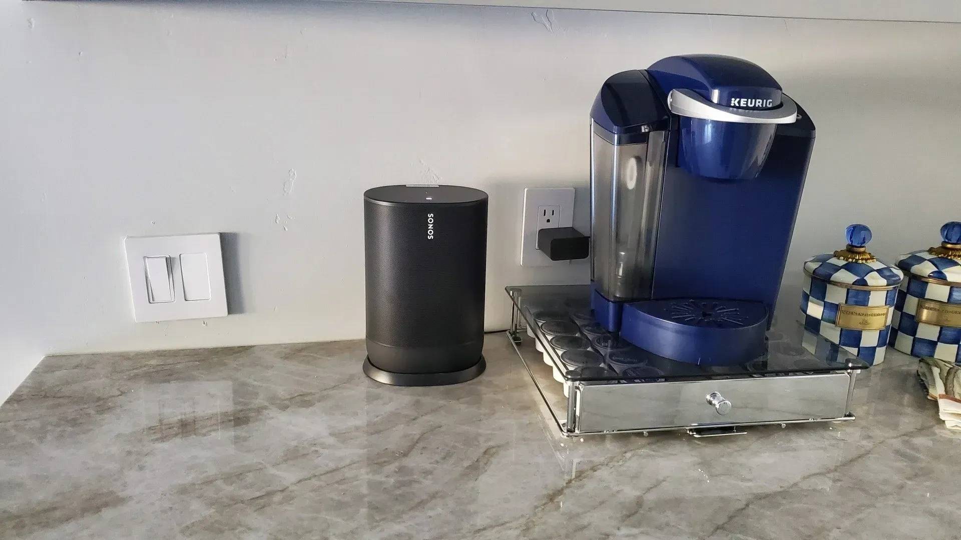 A blue coffee maker is sitting on a counter next to a speaker.