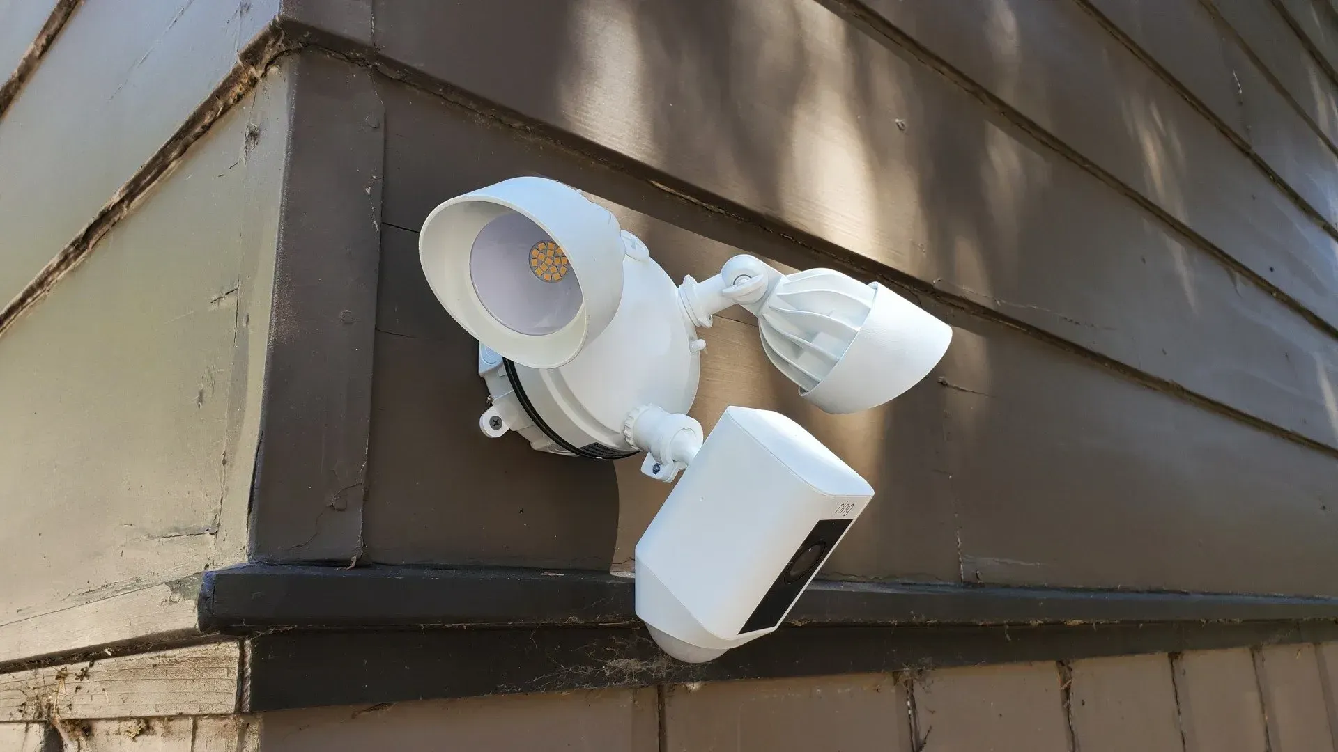 A white flood light is mounted on the side of a house.