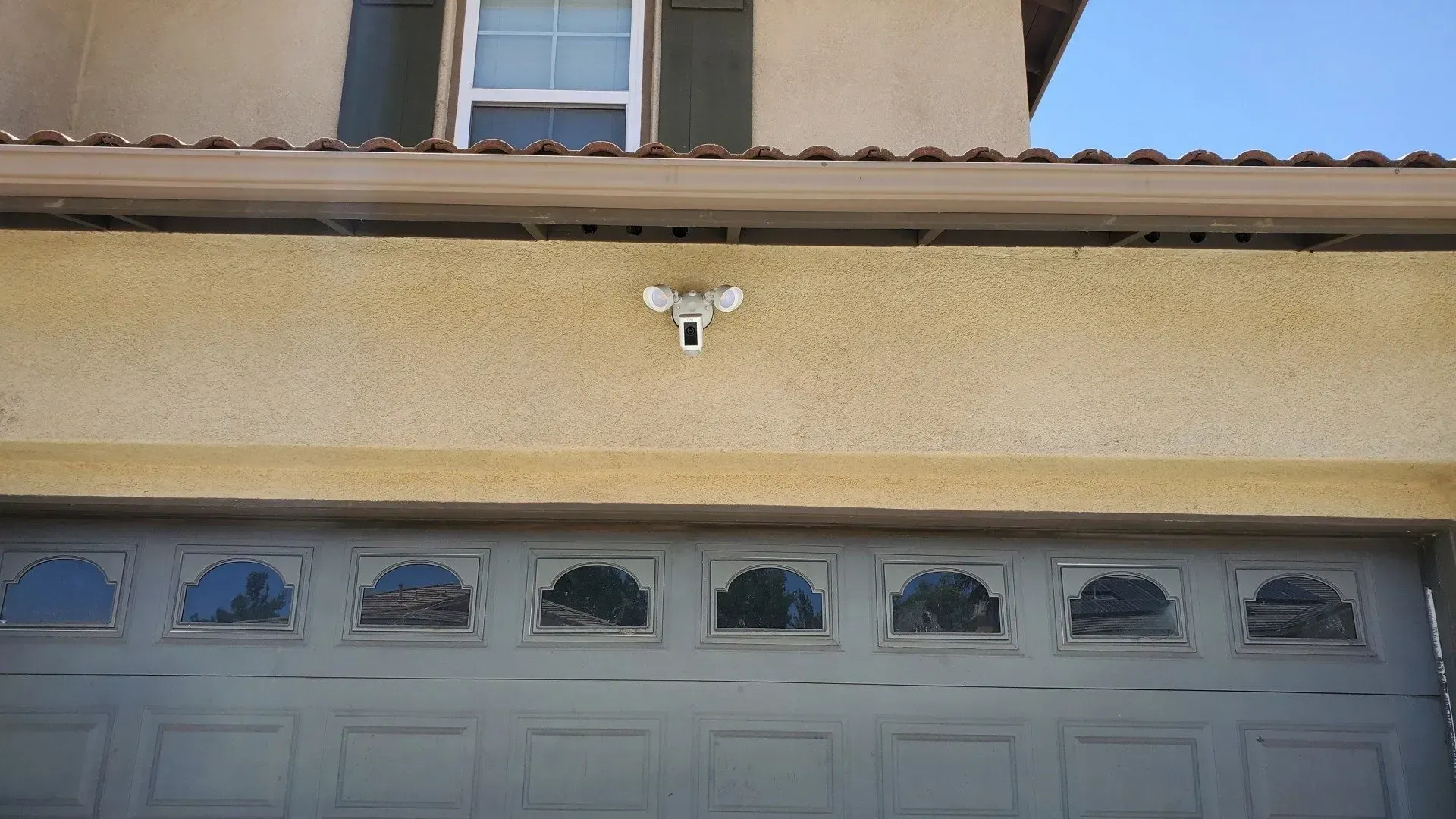A security camera is mounted on the side of a house next to a garage door.