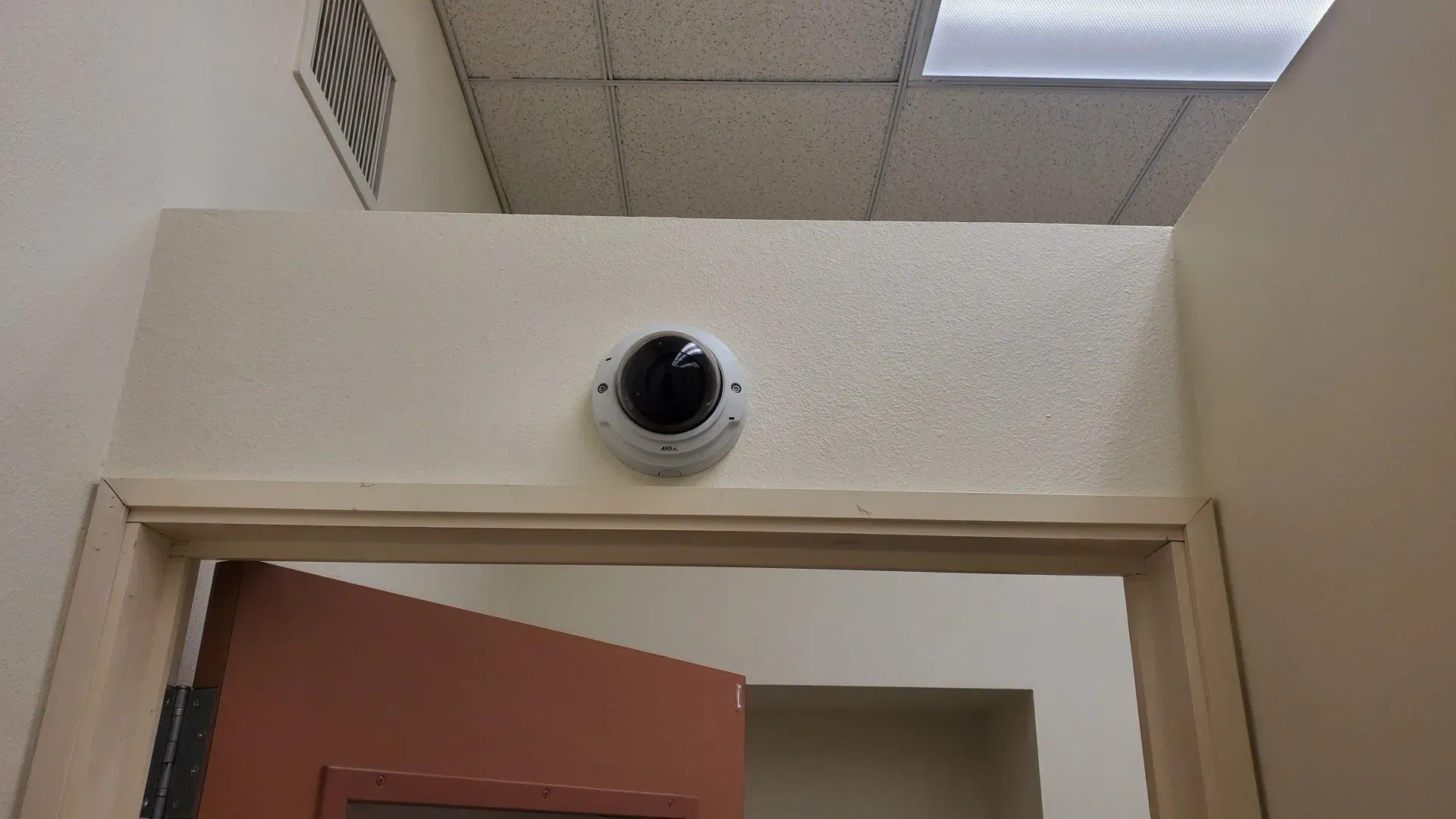 A security camera is mounted on the wall above a door.