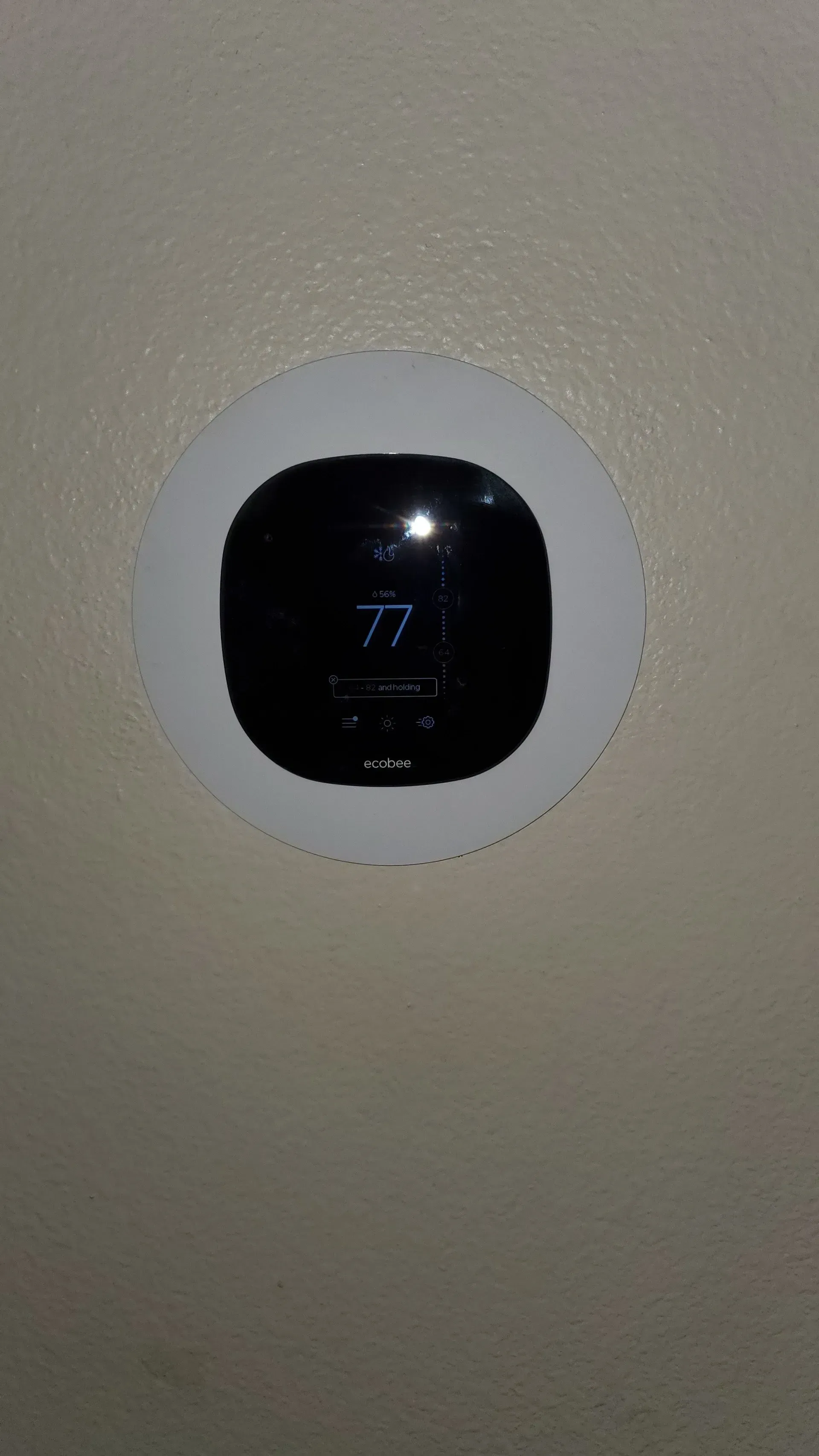 A black thermostat is sitting on a white wall.