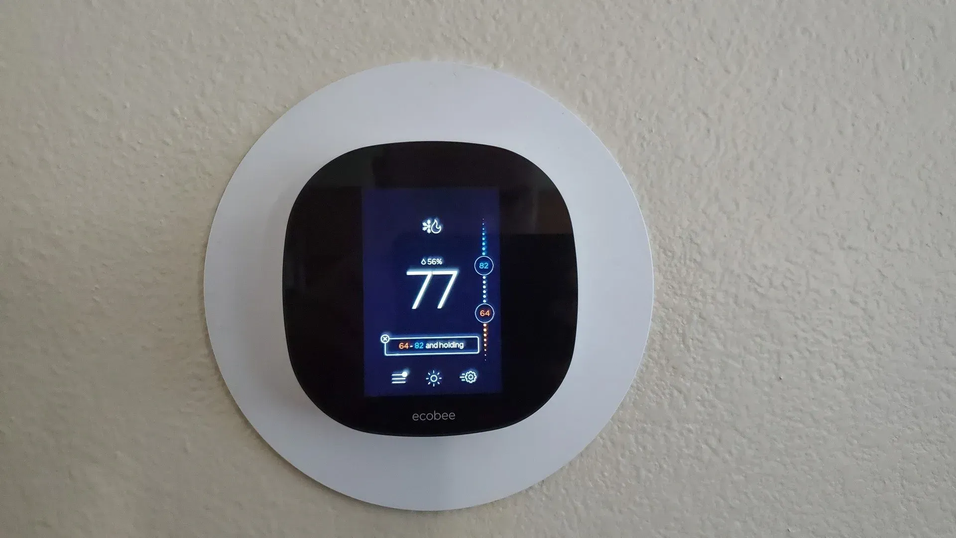 A thermostat is mounted on a wall and the temperature is 77 degrees