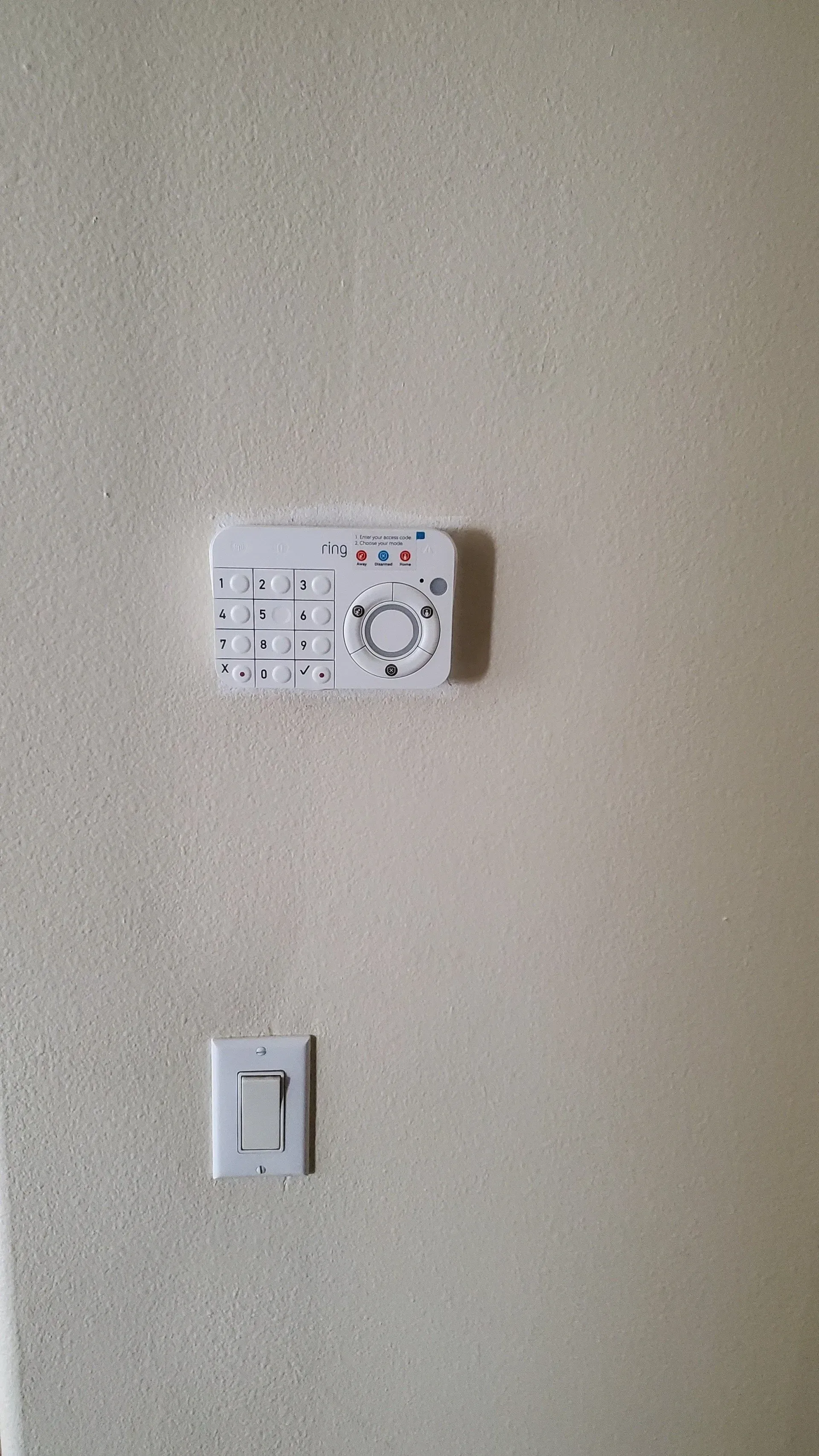 A white thermostat is hanging on a wall next to a light switch.