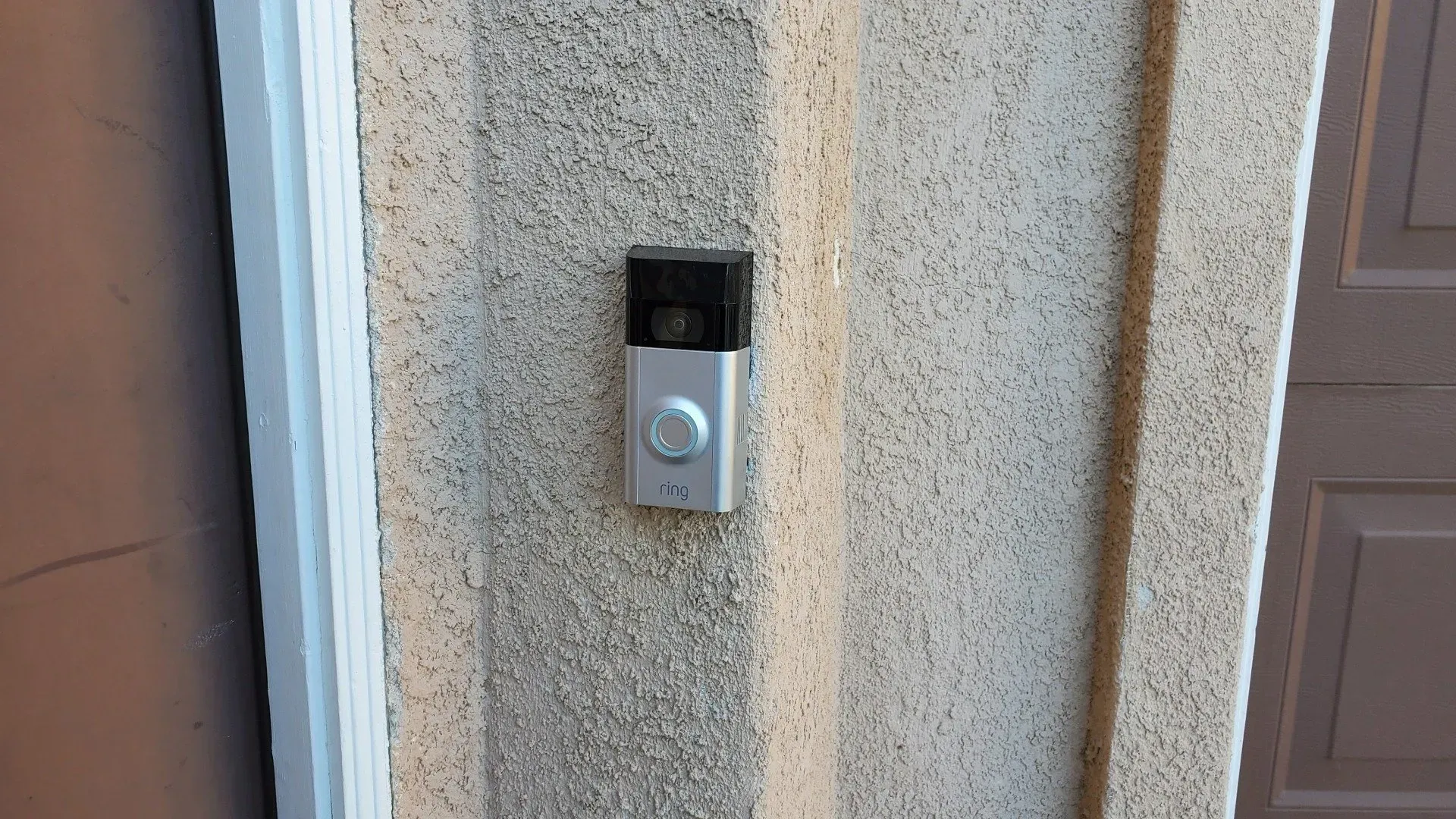 A doorbell is mounted on the side of a building next to a garage door.