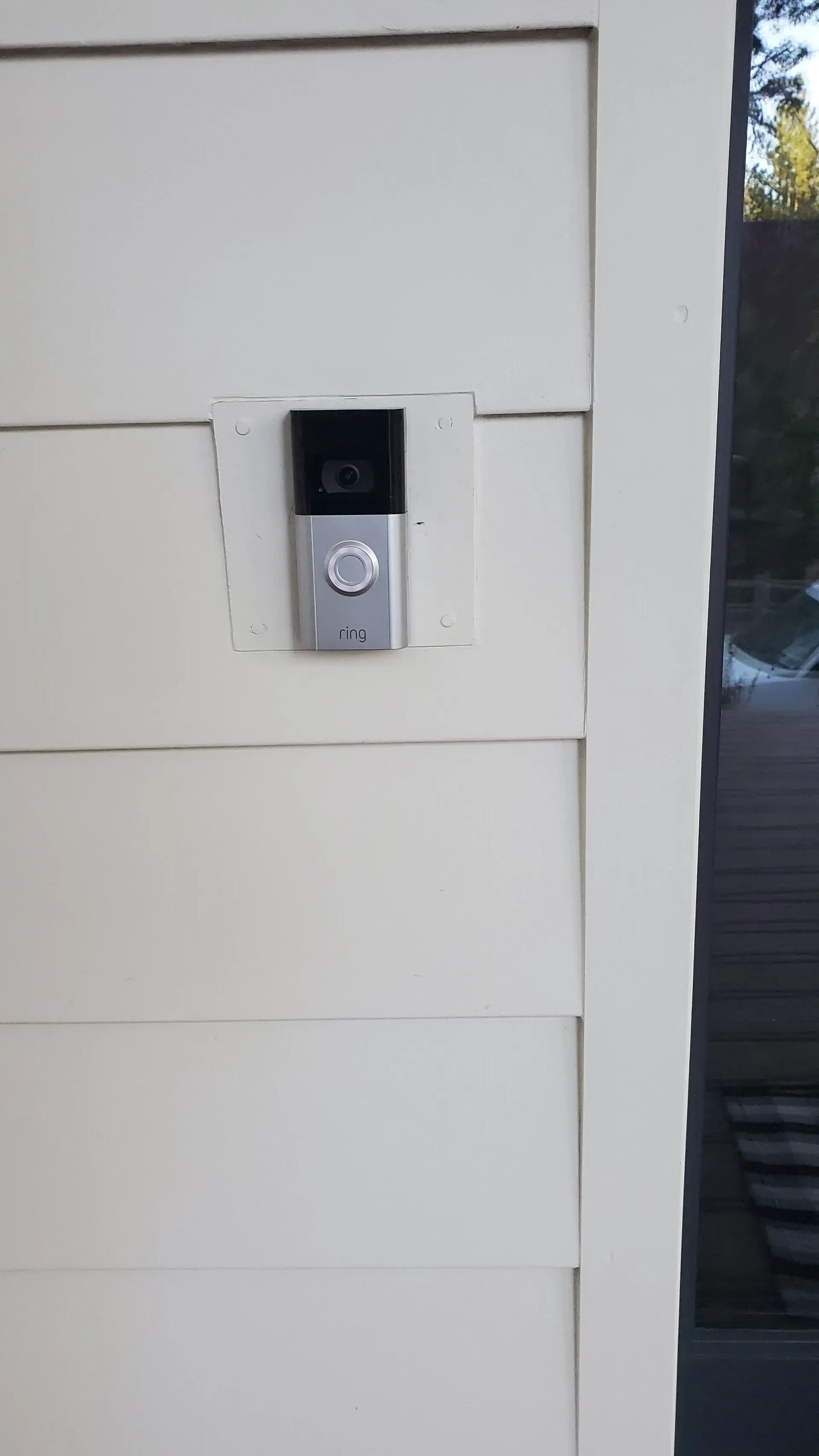 A doorbell is mounted on the side of a white house.