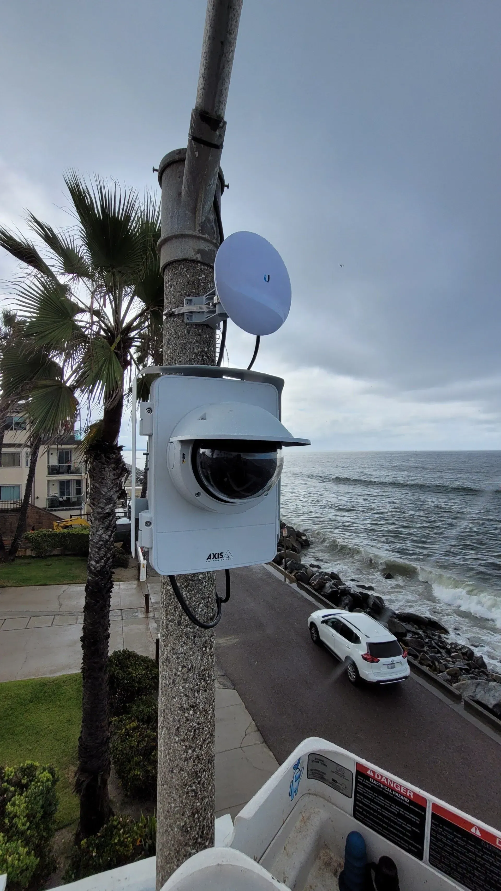 A security camera is mounted on a pole next to the ocean.