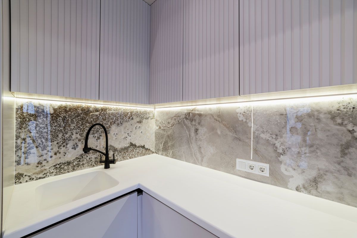 A kitchen with white cabinets , a sink , and a marble counter top.