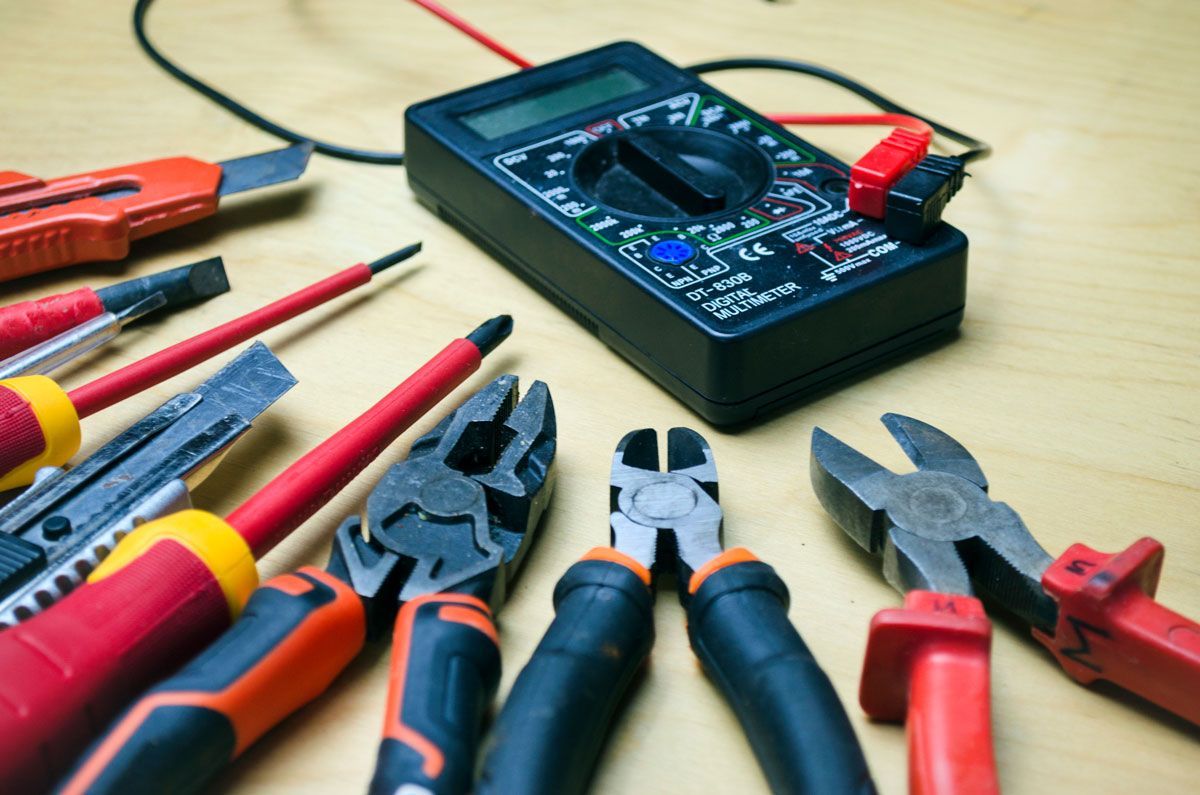 A bunch of tools are on a table including a multimeter and pliers