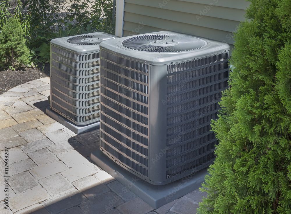 Two air conditioners are sitting on the side of a house.