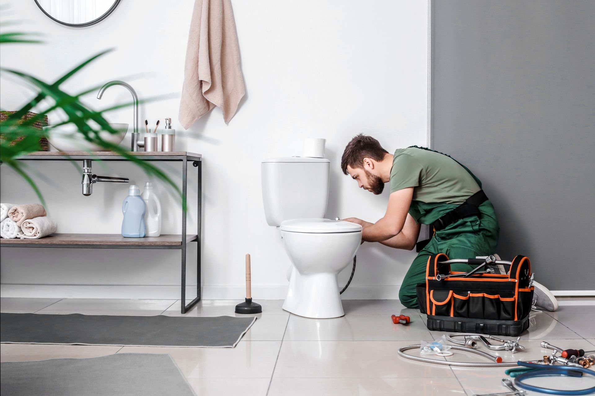 A plumber is fixing a toilet in a bathroom.