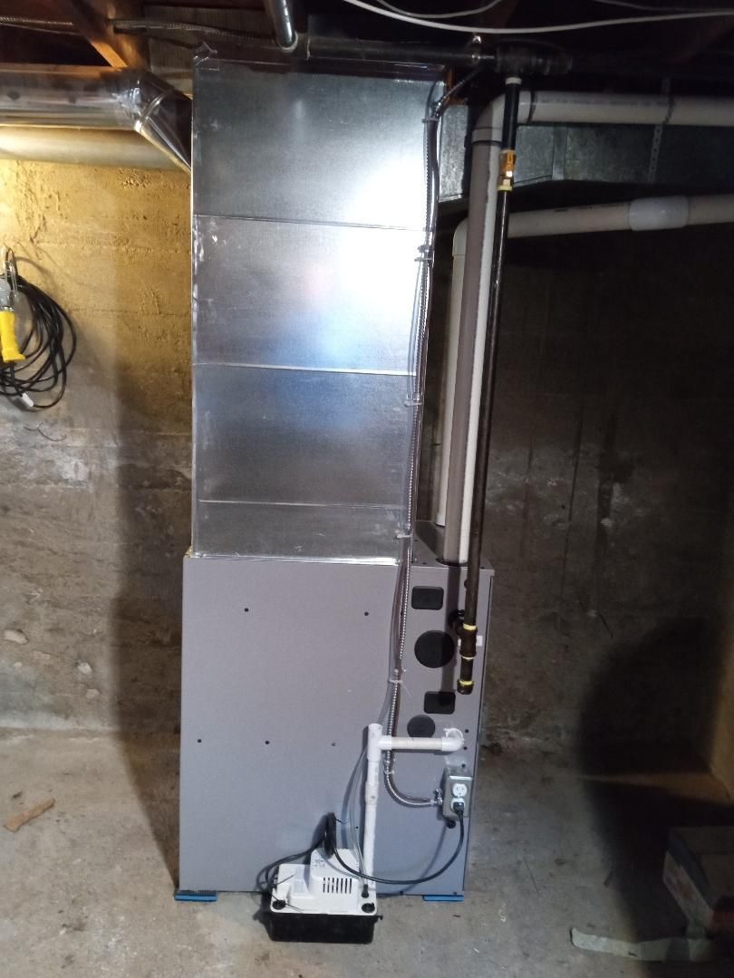A gray air conditioner is sitting in a basement next to a wall.