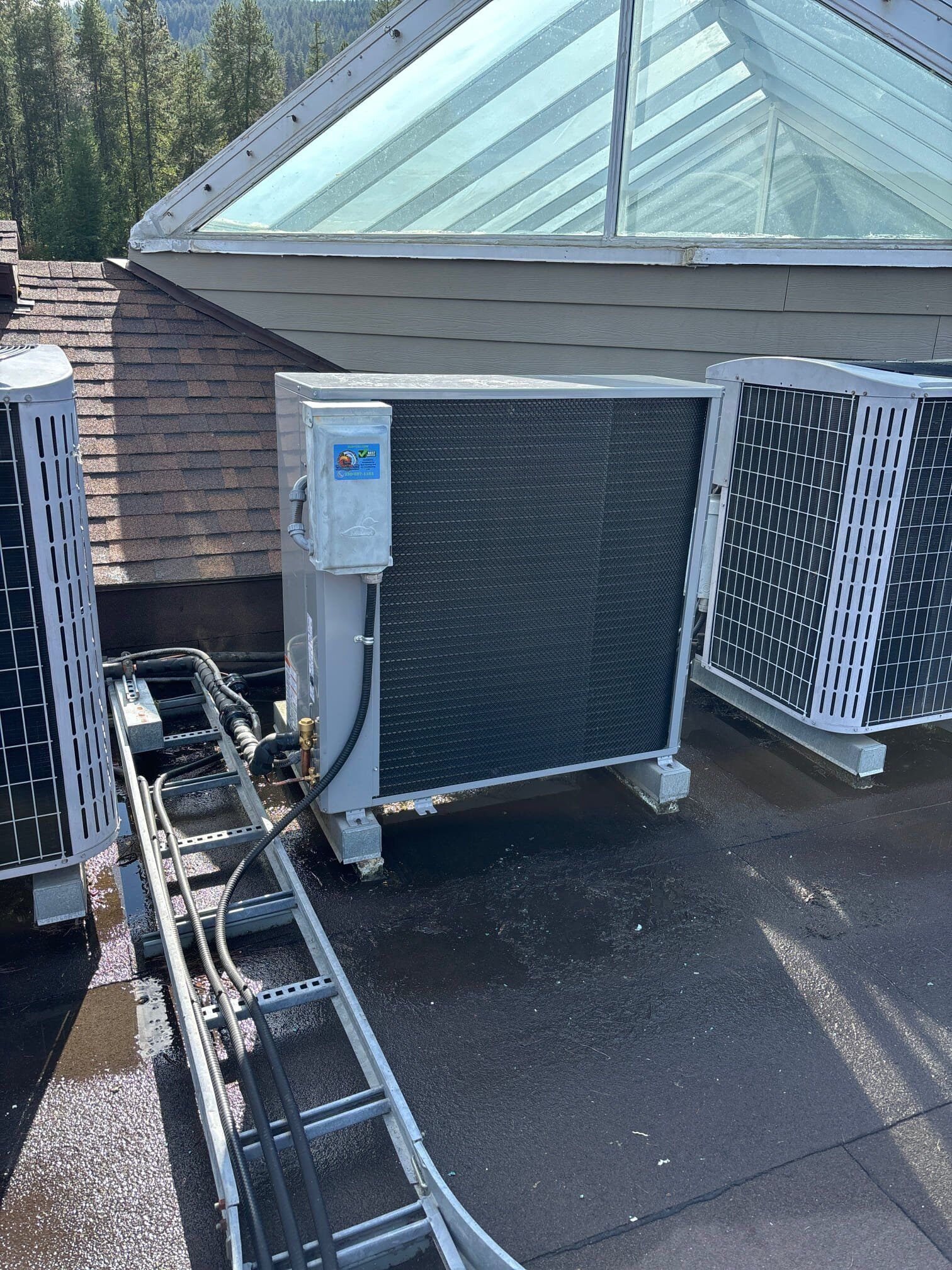 Two air conditioners are sitting on top of a roof next to a ladder.