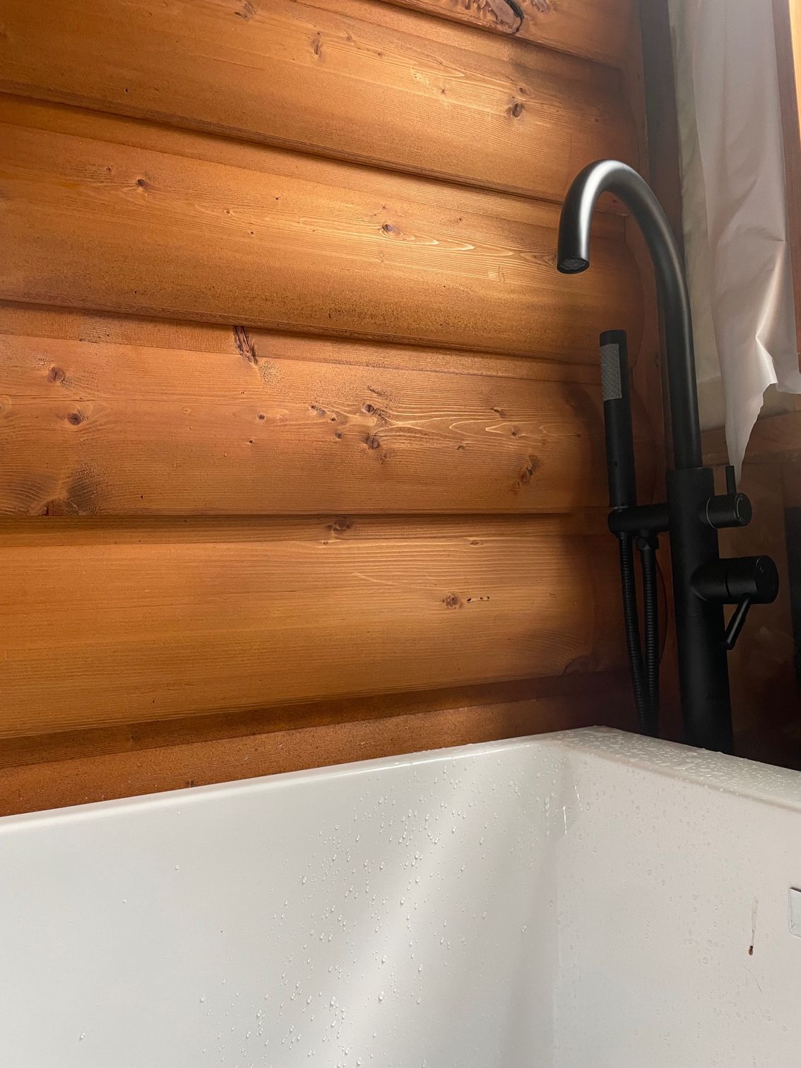 A white bathtub with a black faucet in front of a wooden wall.