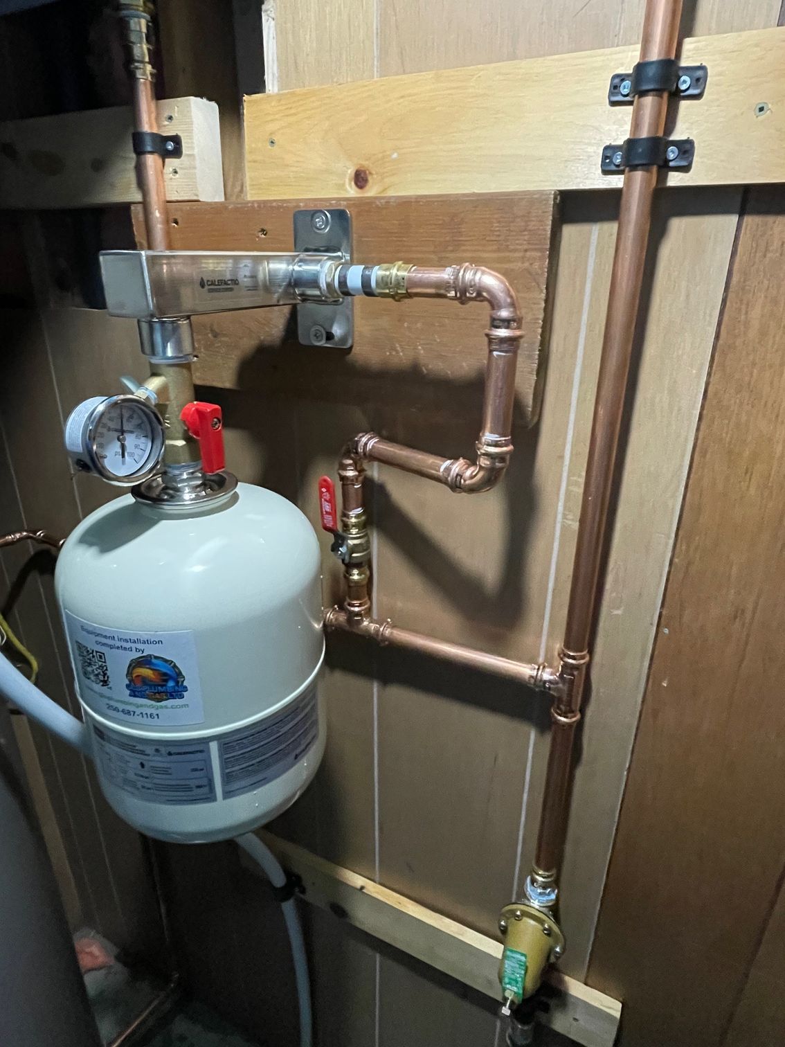 A propane tank is attached to a copper pipe in a room.