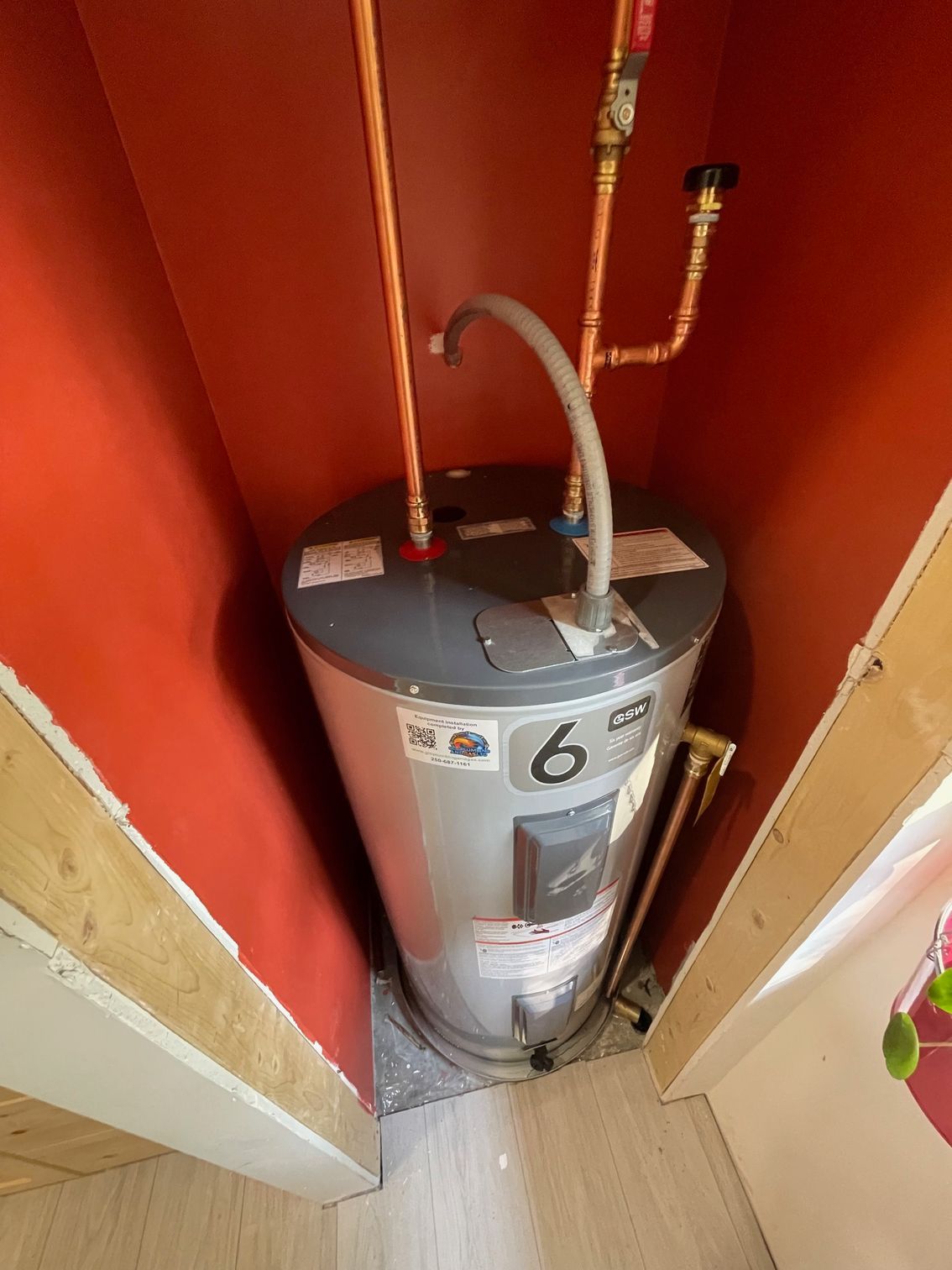 A water heater is sitting in a corner of a room next to a red wall.