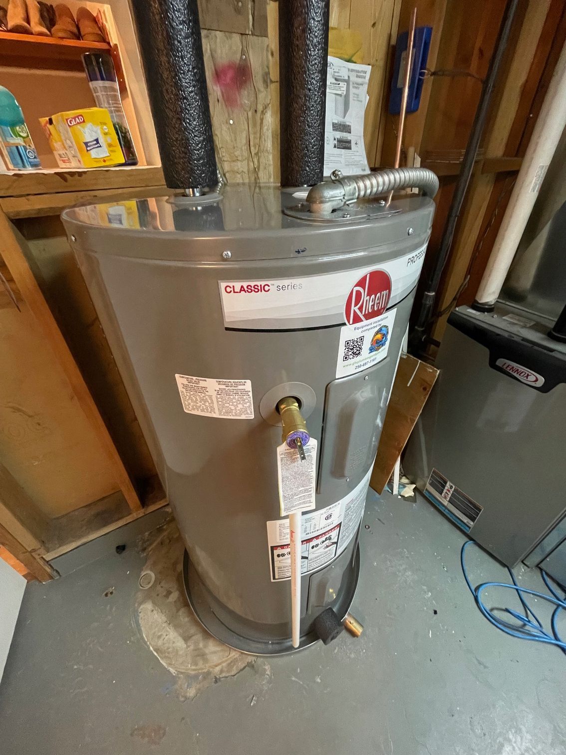 A gray water heater is sitting in a basement next to a wooden wall.