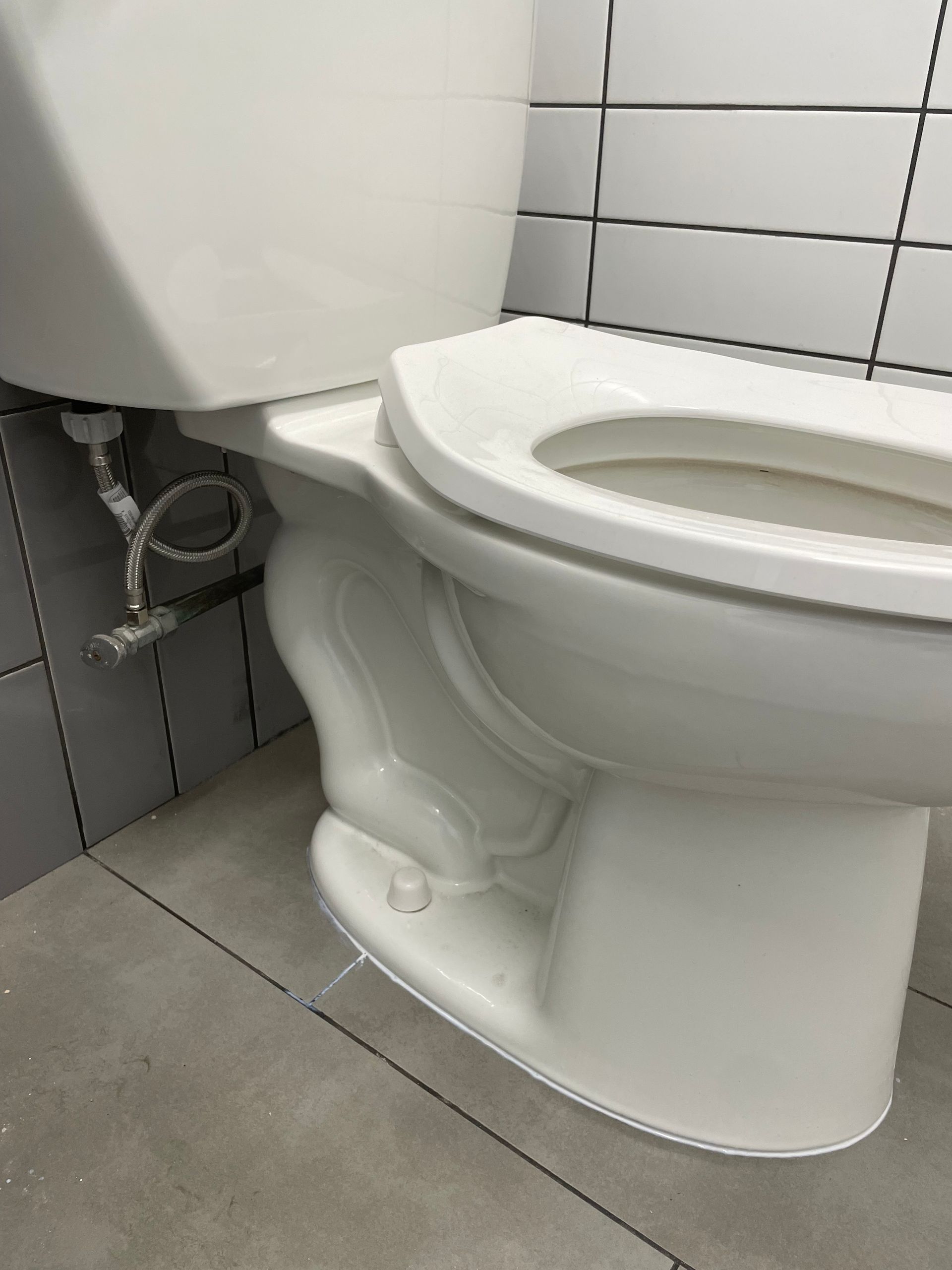 A white toilet is sitting on a tiled floor in a bathroom.