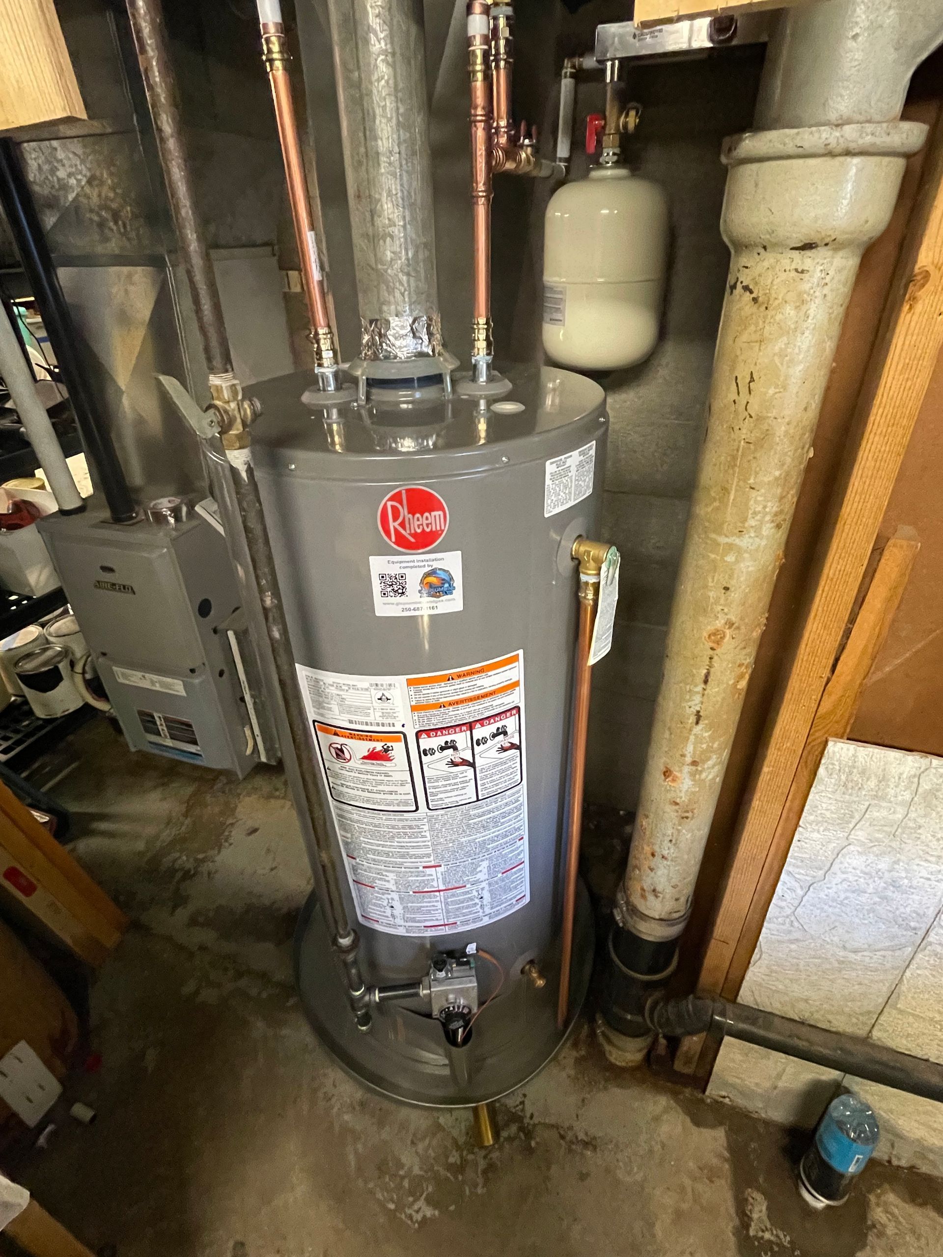 A water heater is sitting in a basement next to a furnace.