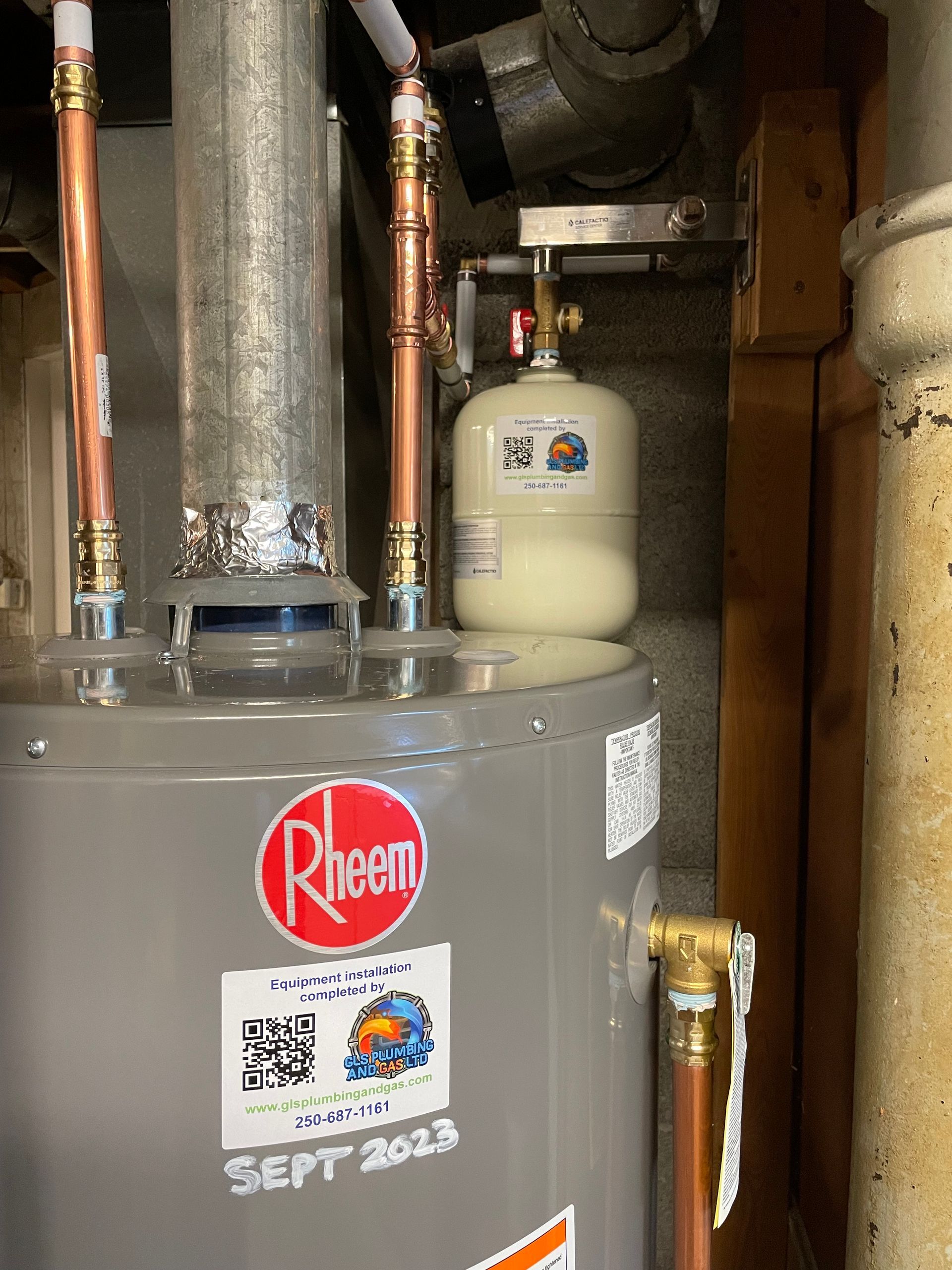 A rheem water heater is sitting in a basement next to a copper pipe.