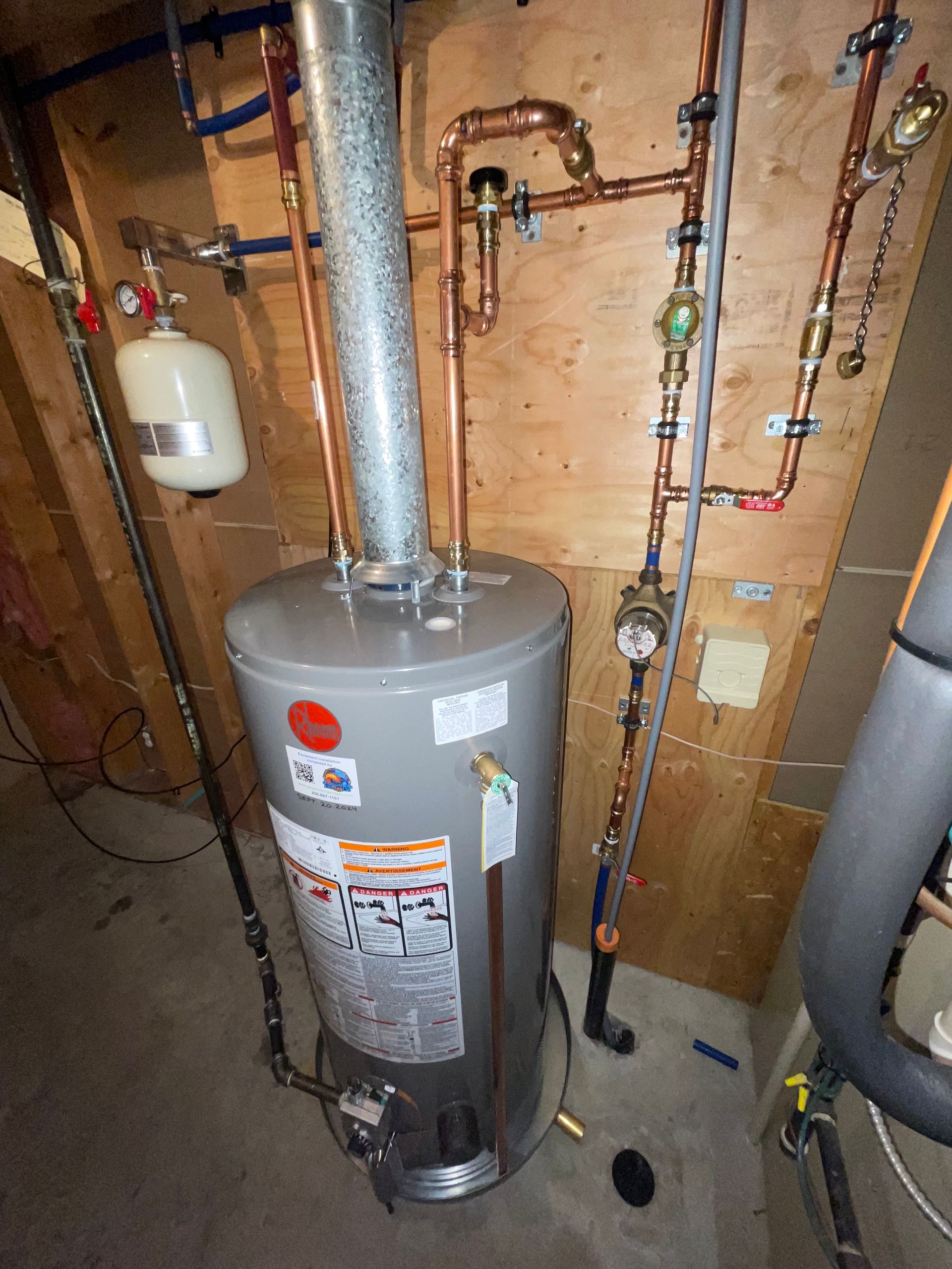 A water heater is sitting in a basement next to pipes.