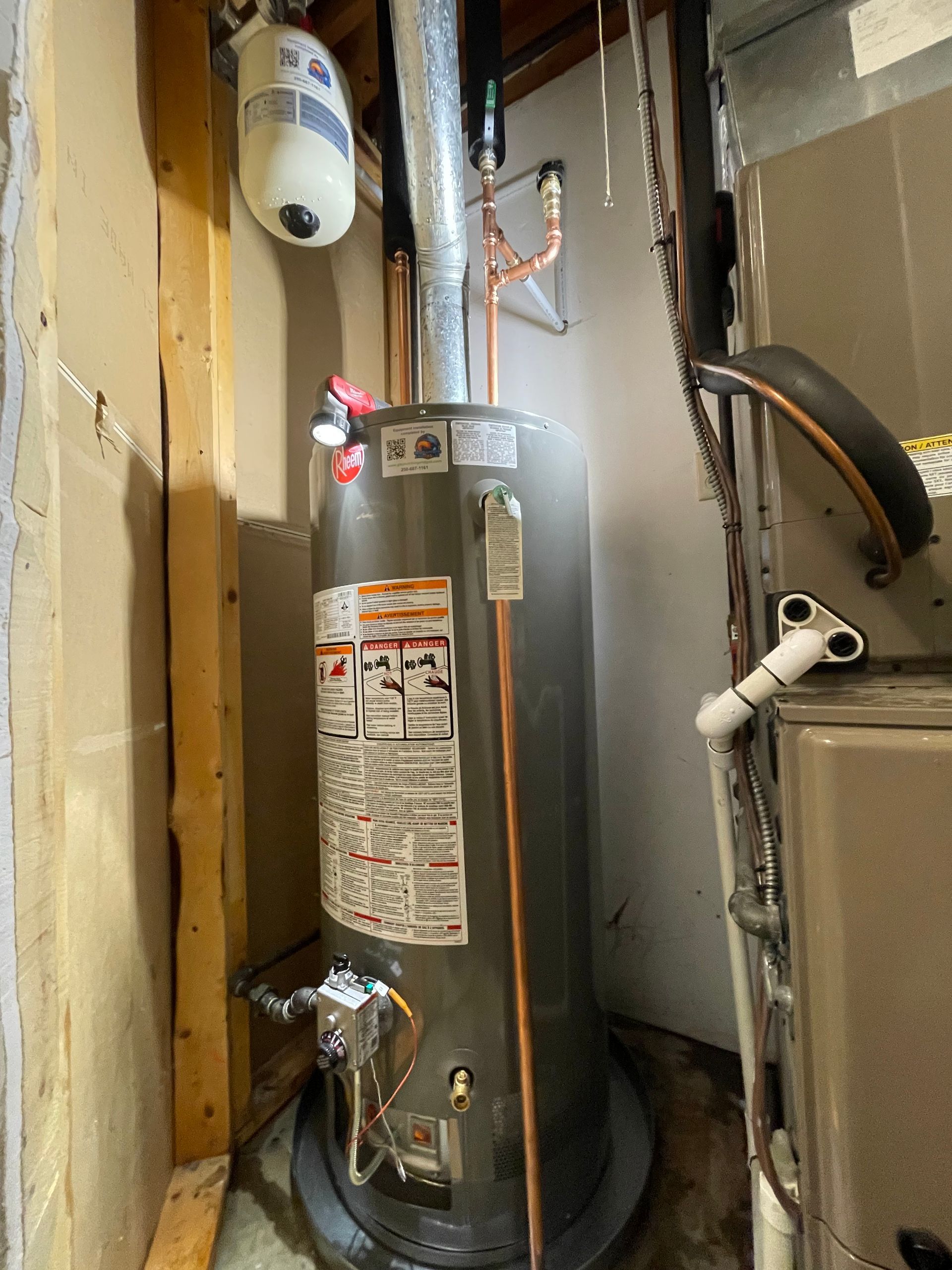 A water heater is sitting in a room next to a furnace.