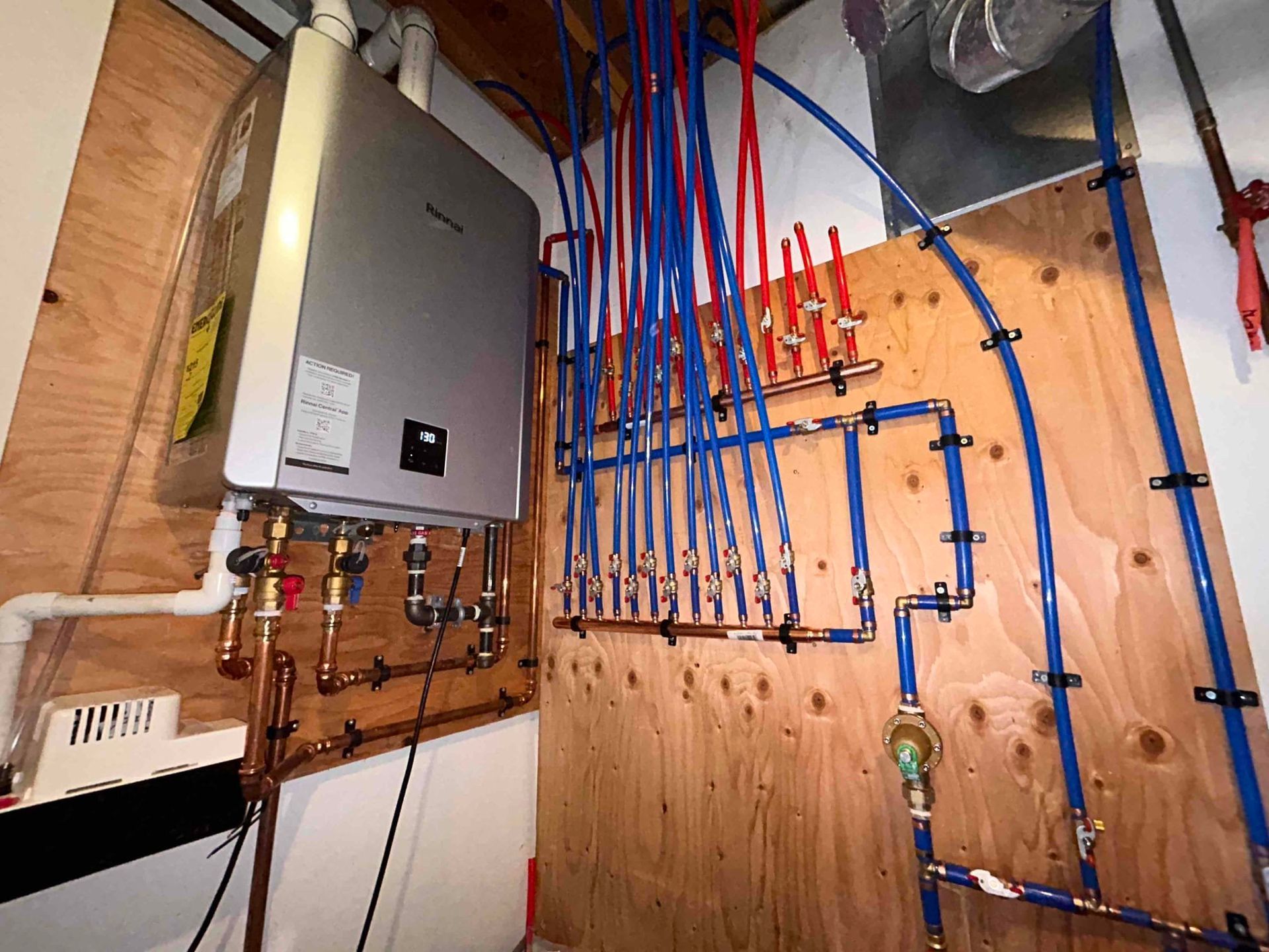 A room with a boiler and pipes hanging from the ceiling.
