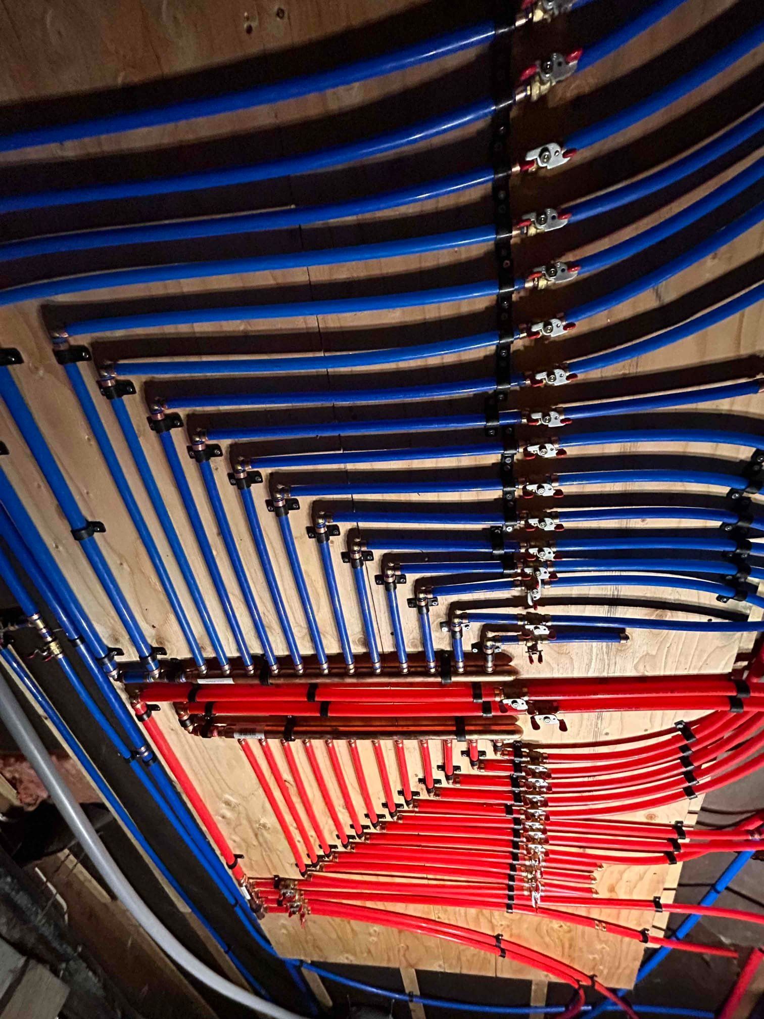 Blue and red PEX tubing for a radiant heating system, connected to manifolds, installed on a wooden subfloor.