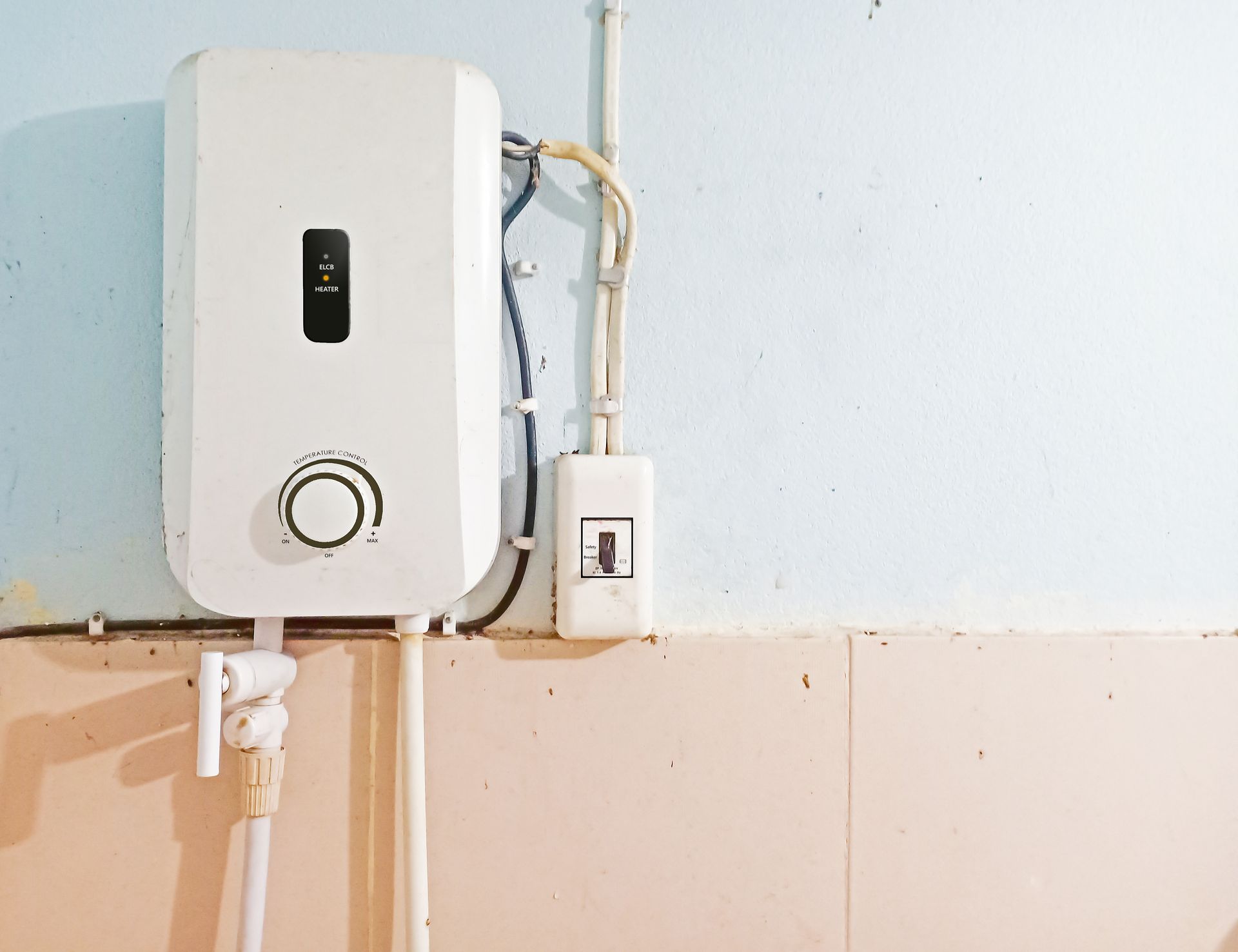 A white water heater is attached to a wall in a bathroom.