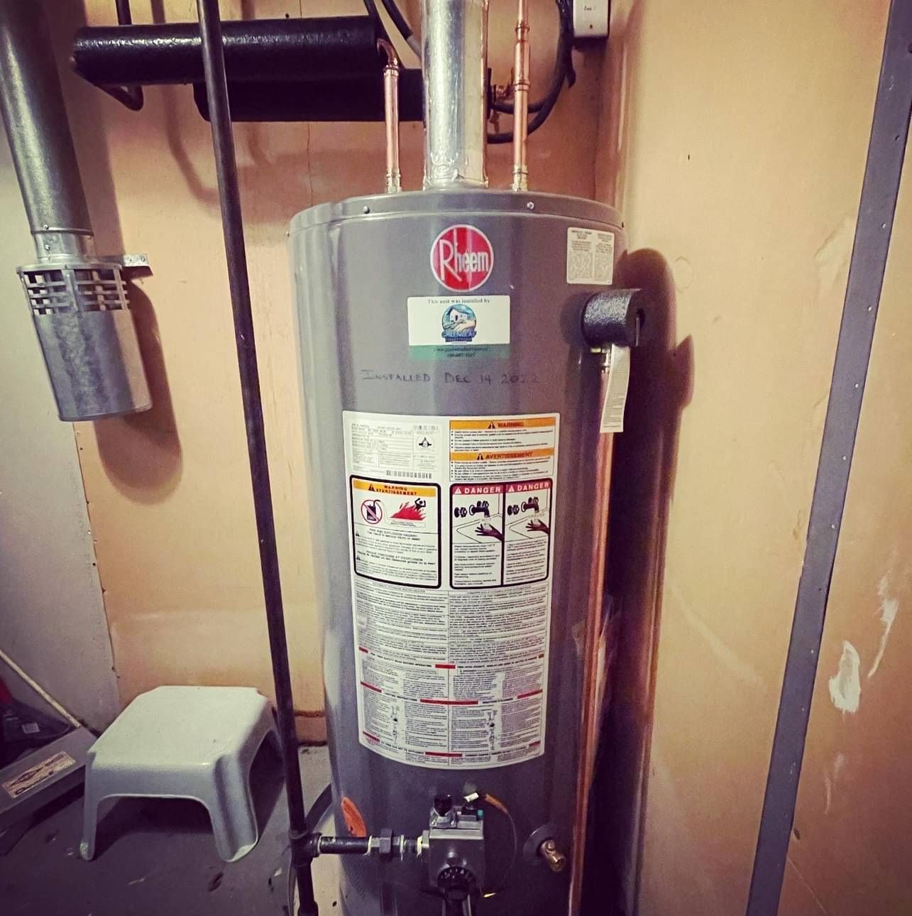 A rheem water heater is sitting in a room next to a stool