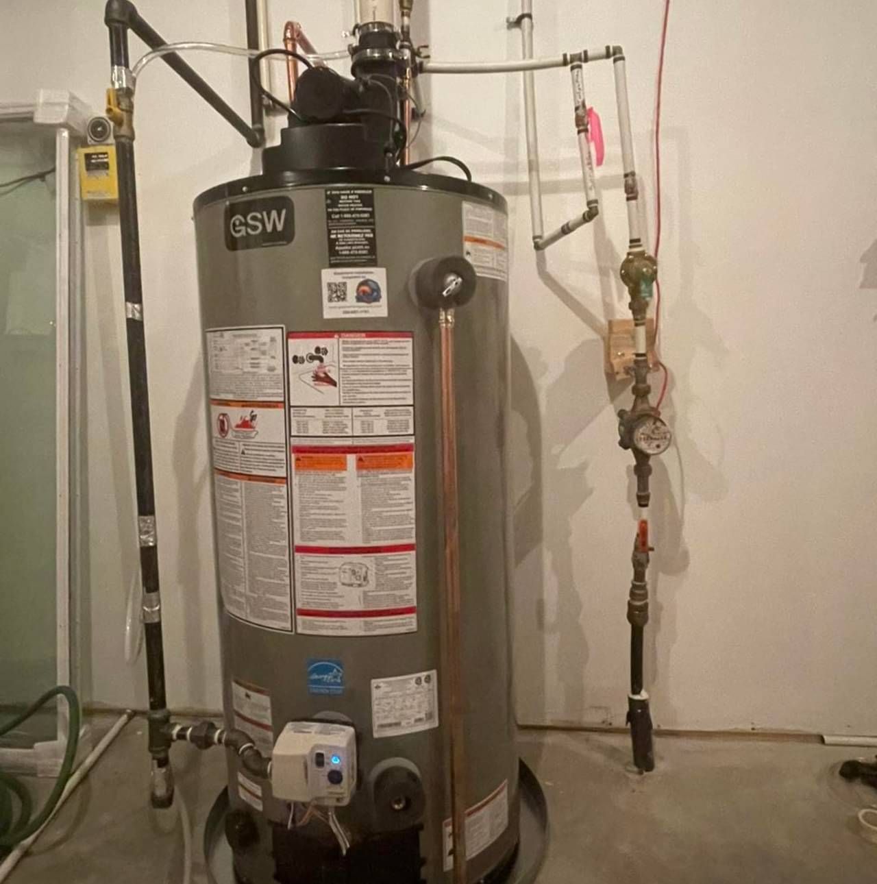 A water heater is sitting in a basement next to a wall.