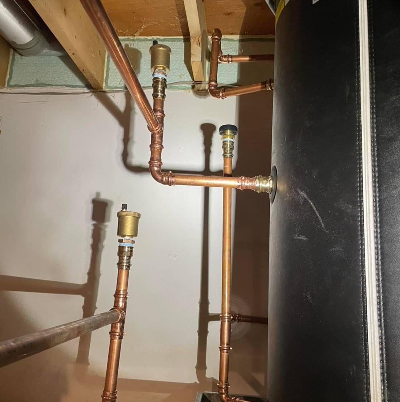 Copper pipes are connected to a black tank in a room