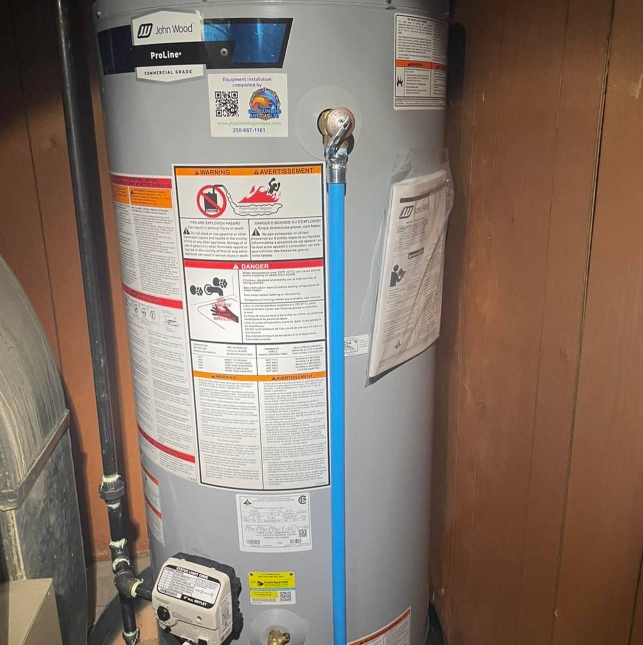 A water heater is sitting in a room next to a wooden wall.