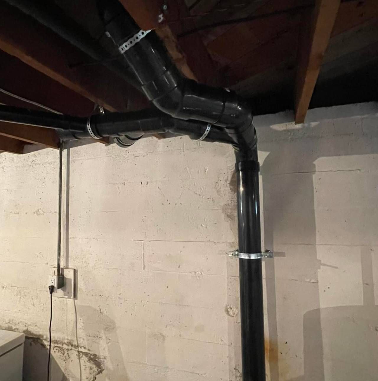 A black pipe is hanging from the ceiling in a basement