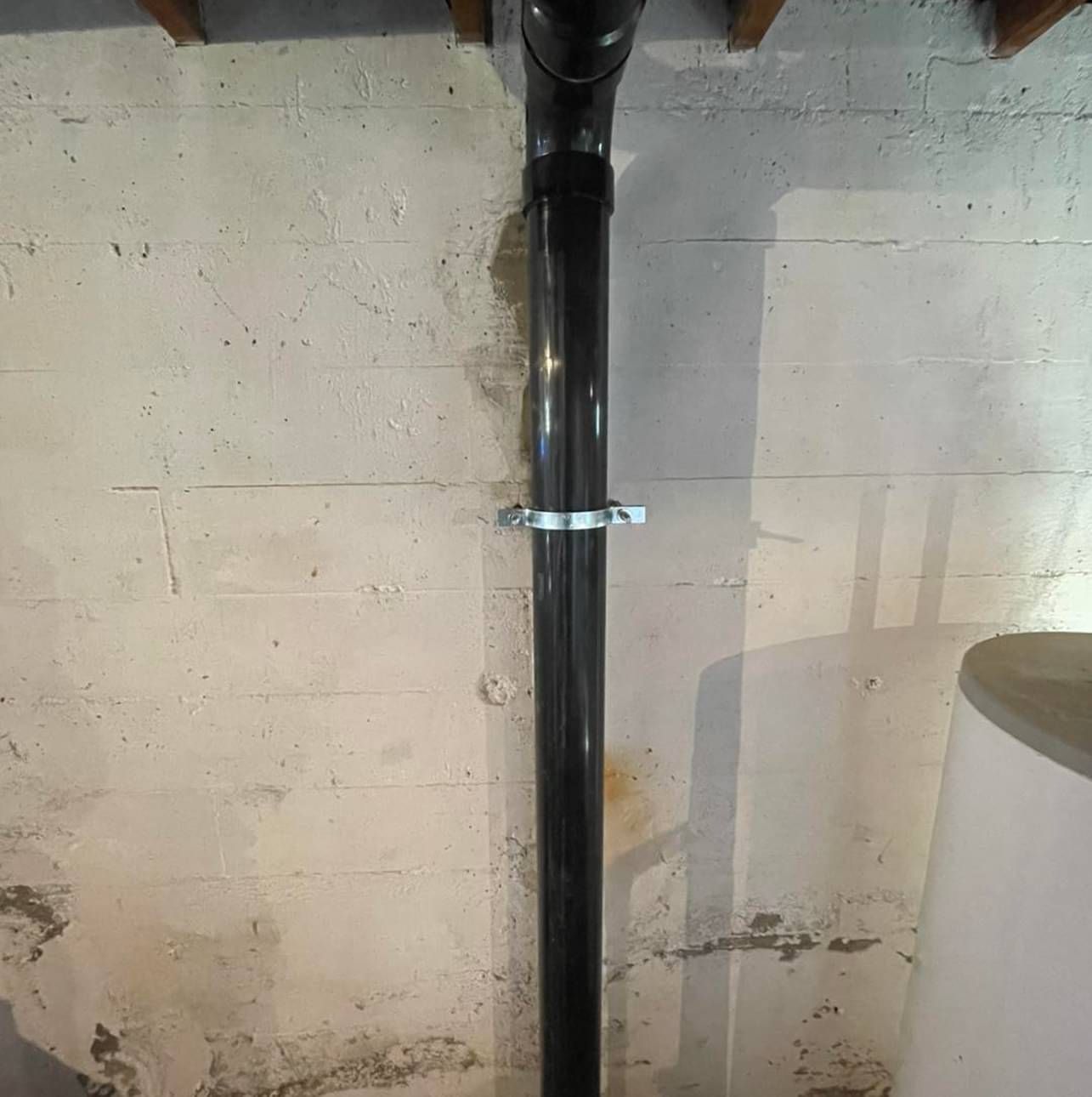 A black pipe is attached to a white wall in a basement.