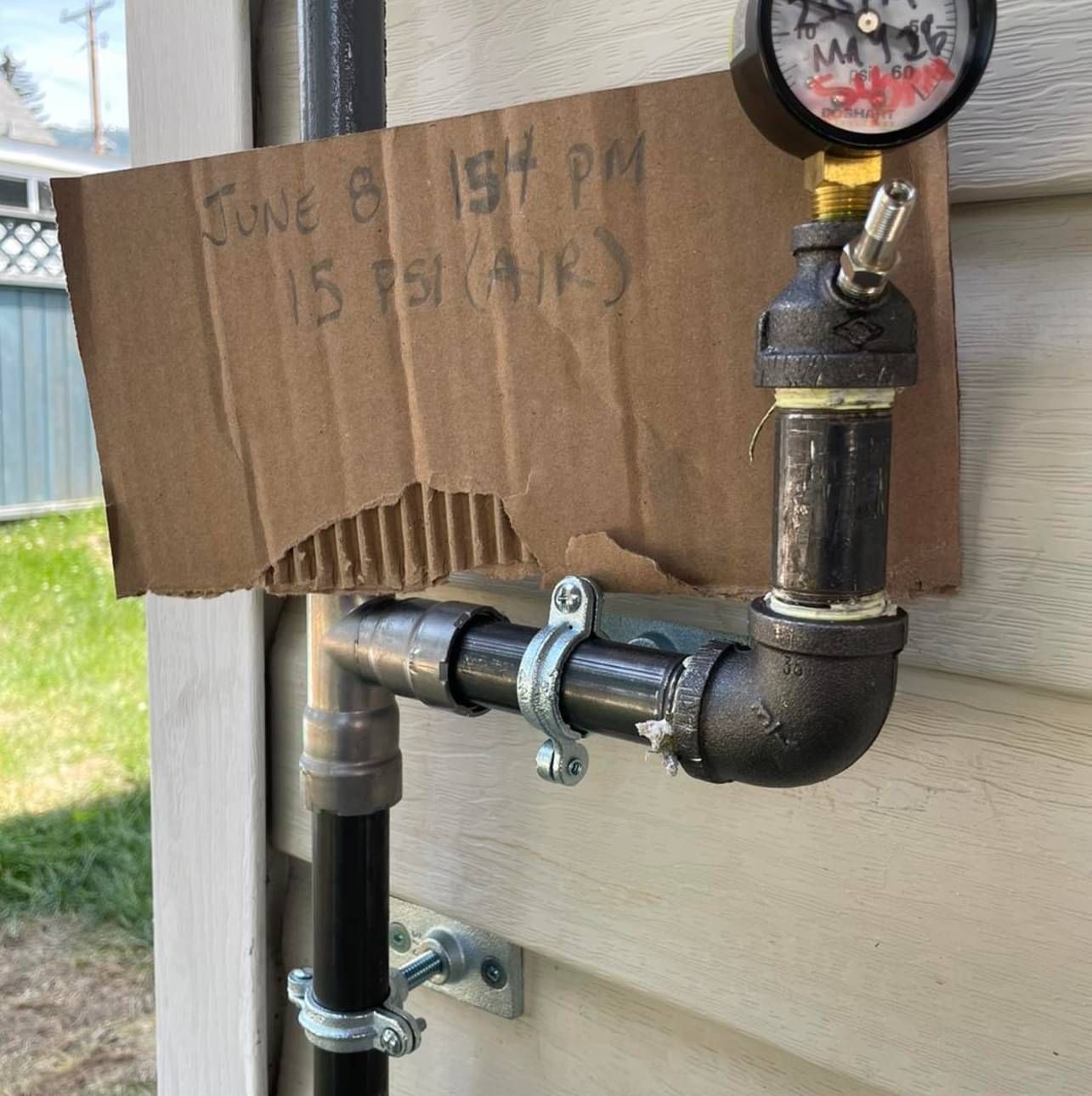 A cardboard sign is attached to a pipe on the side of a house