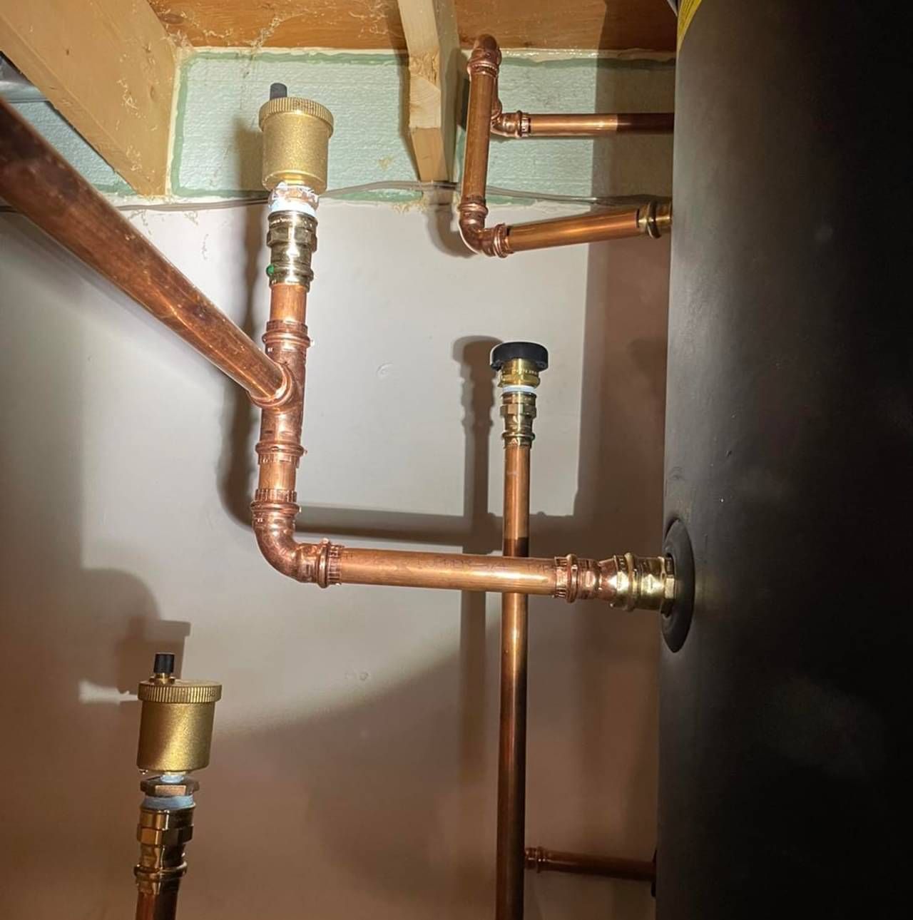Copper pipes are connected to a black tank in a room.