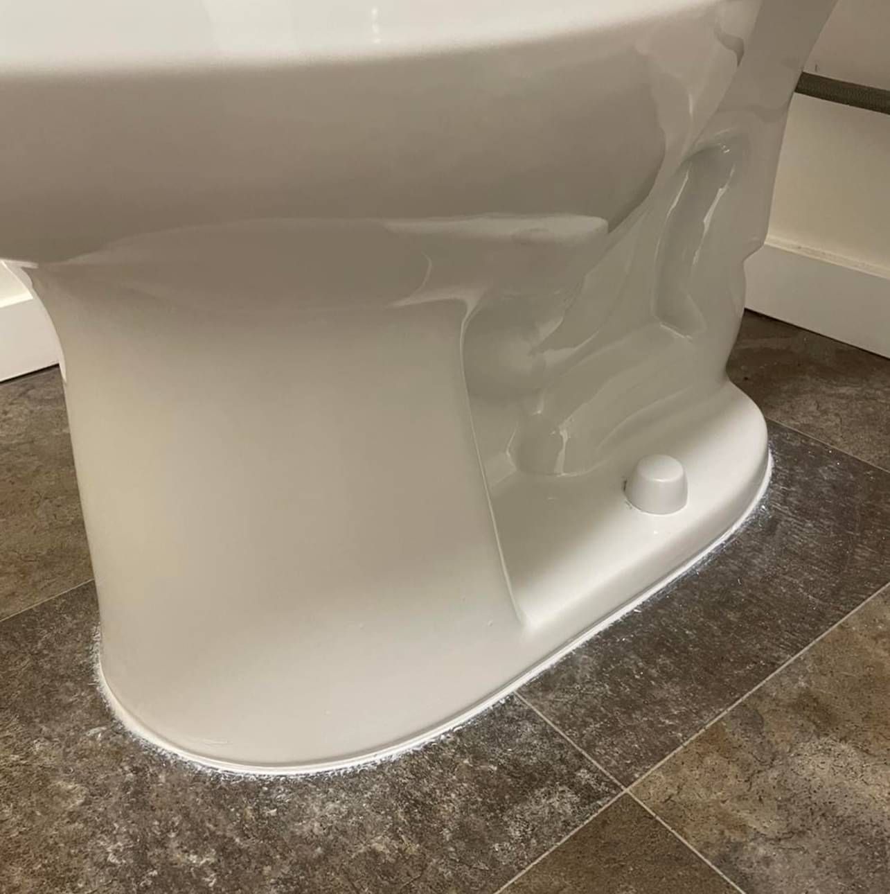 A white toilet is sitting on a tiled floor in a bathroom.