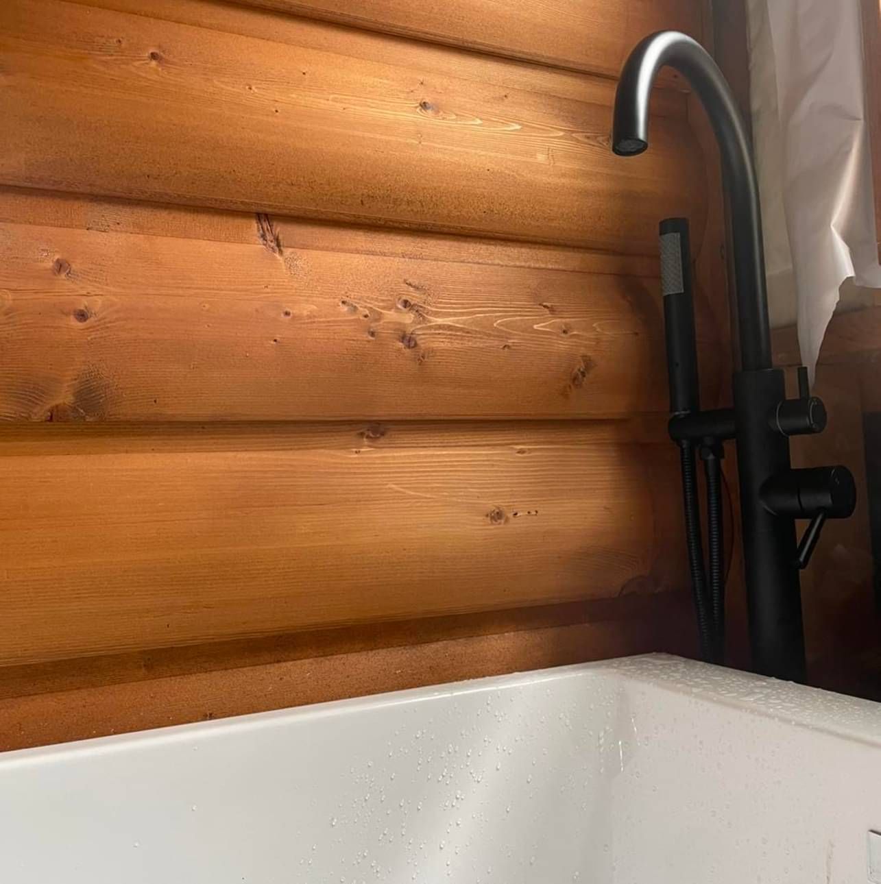 A bathtub with a black faucet in front of a wooden wall.