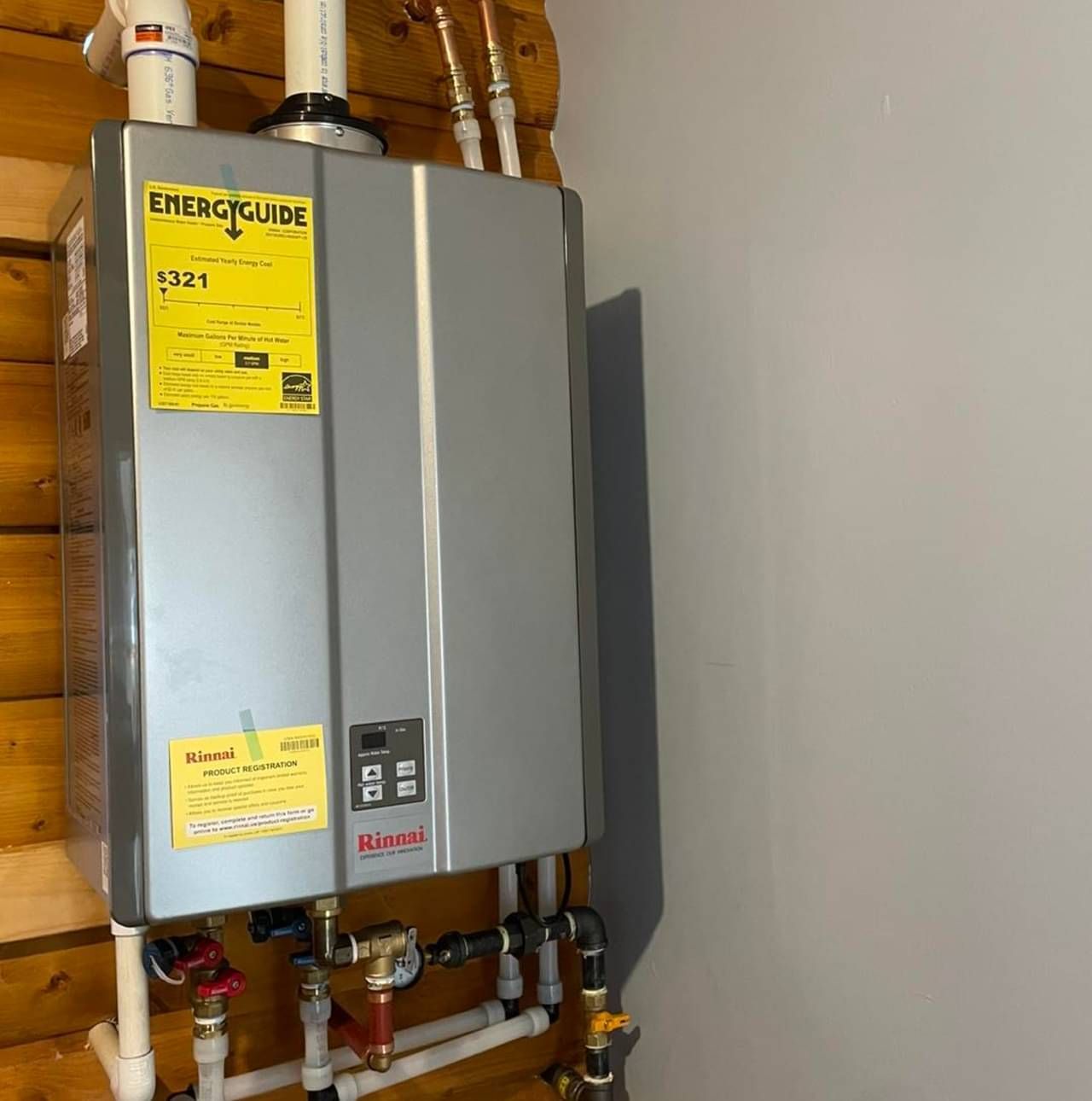 A water heater is hanging on a wall next to pipes.