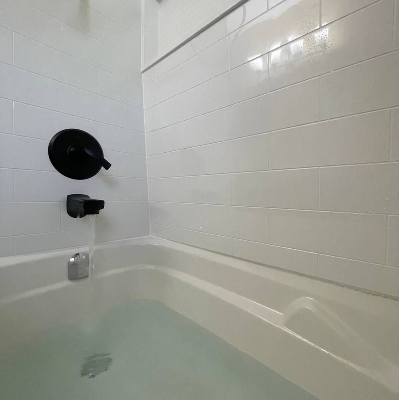 A bathtub filled with water in a bathroom with white tiles.